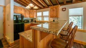 A kitchen with wooden cabinets, granite countertops, and a built-in island with bar stools. - Timbers at Island Park Village Resort (Island Park)