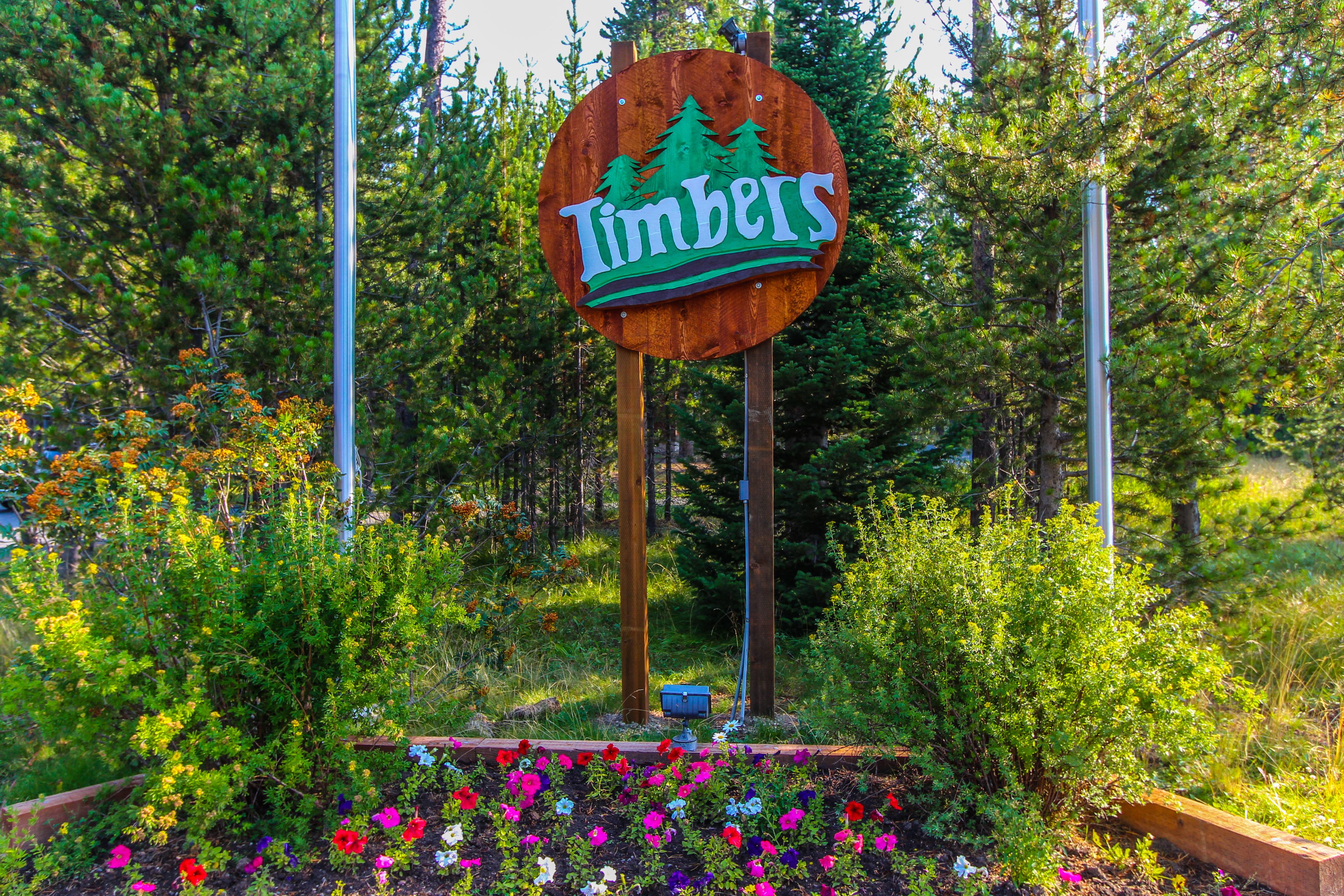 Et træskilt med ordet "Timbers" omgivet af farverige blomster og grønne planter.