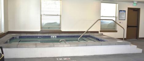 Zona de spa con un jacuzzi, un cartel que prohíbe correr y una escalera que conduce a un ascensor.