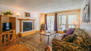 A cozy living room with a fireplace, wooden furniture, and large windows. - Timbers at Island Park Village Resort (Island Park)