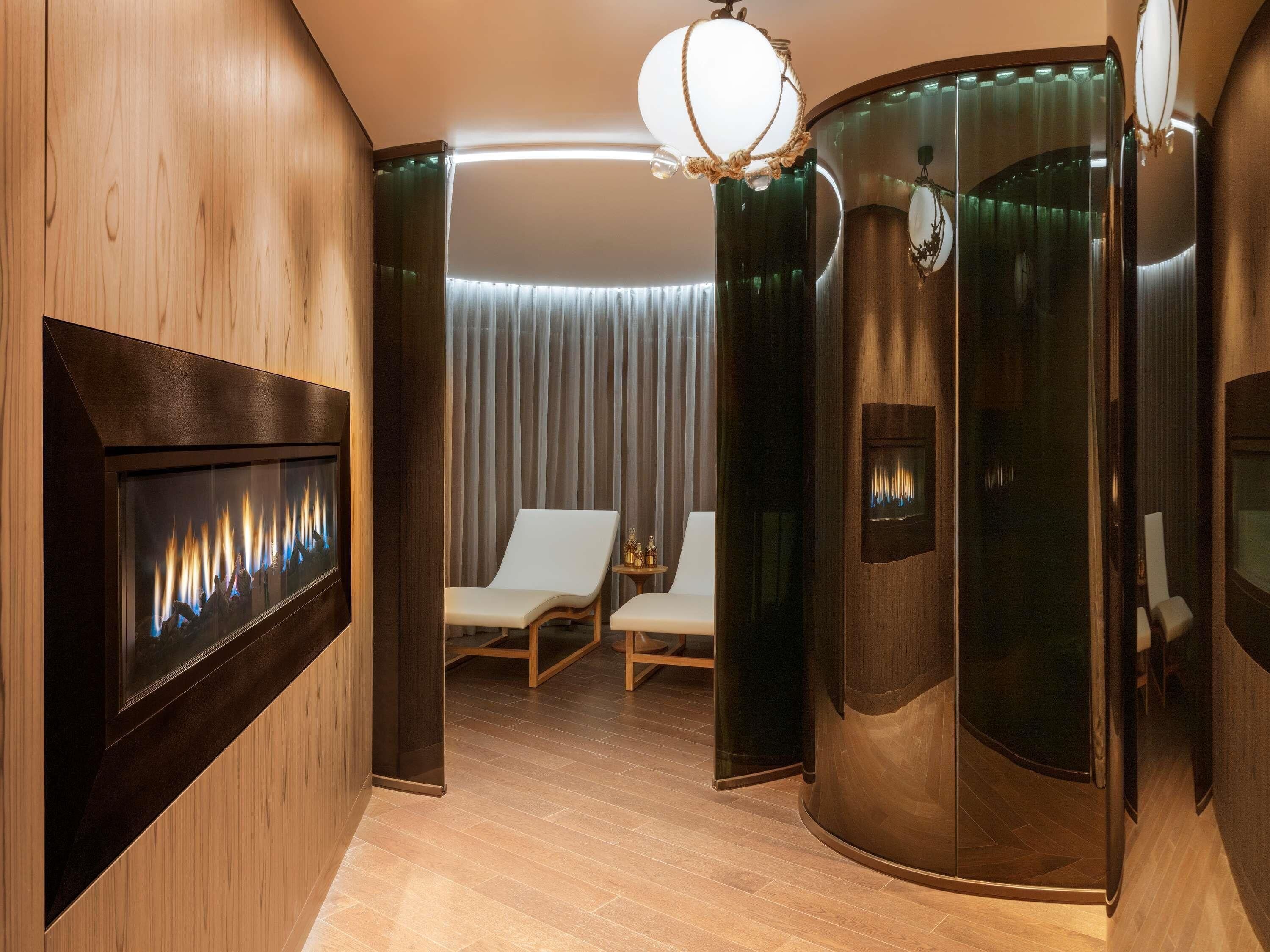 A modern room with a fireplace, two lounge chairs, a glass partition, and a chandelier.