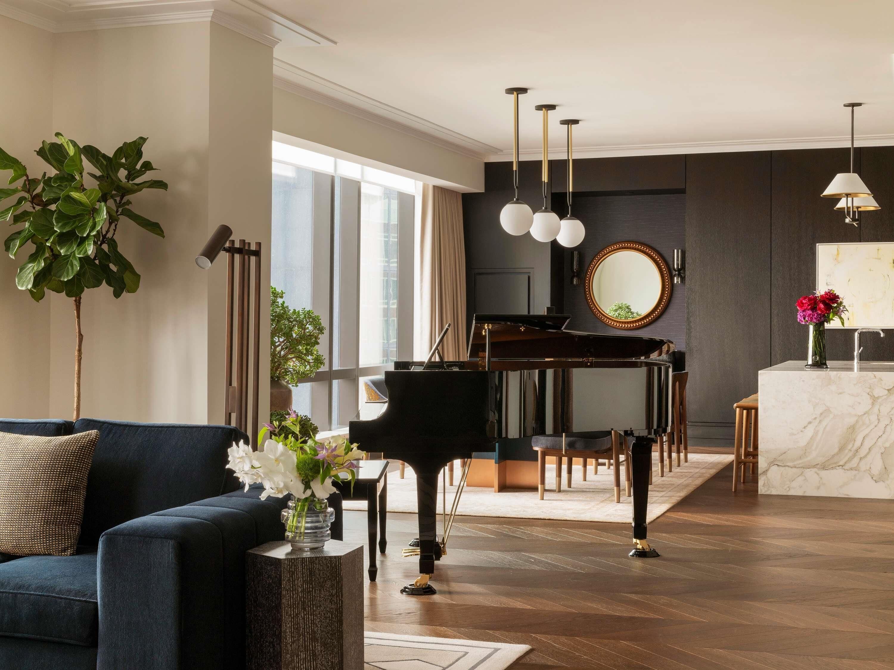 A modern living room with a grand piano, a sofa, a coffee table, and a large window providing natural light.