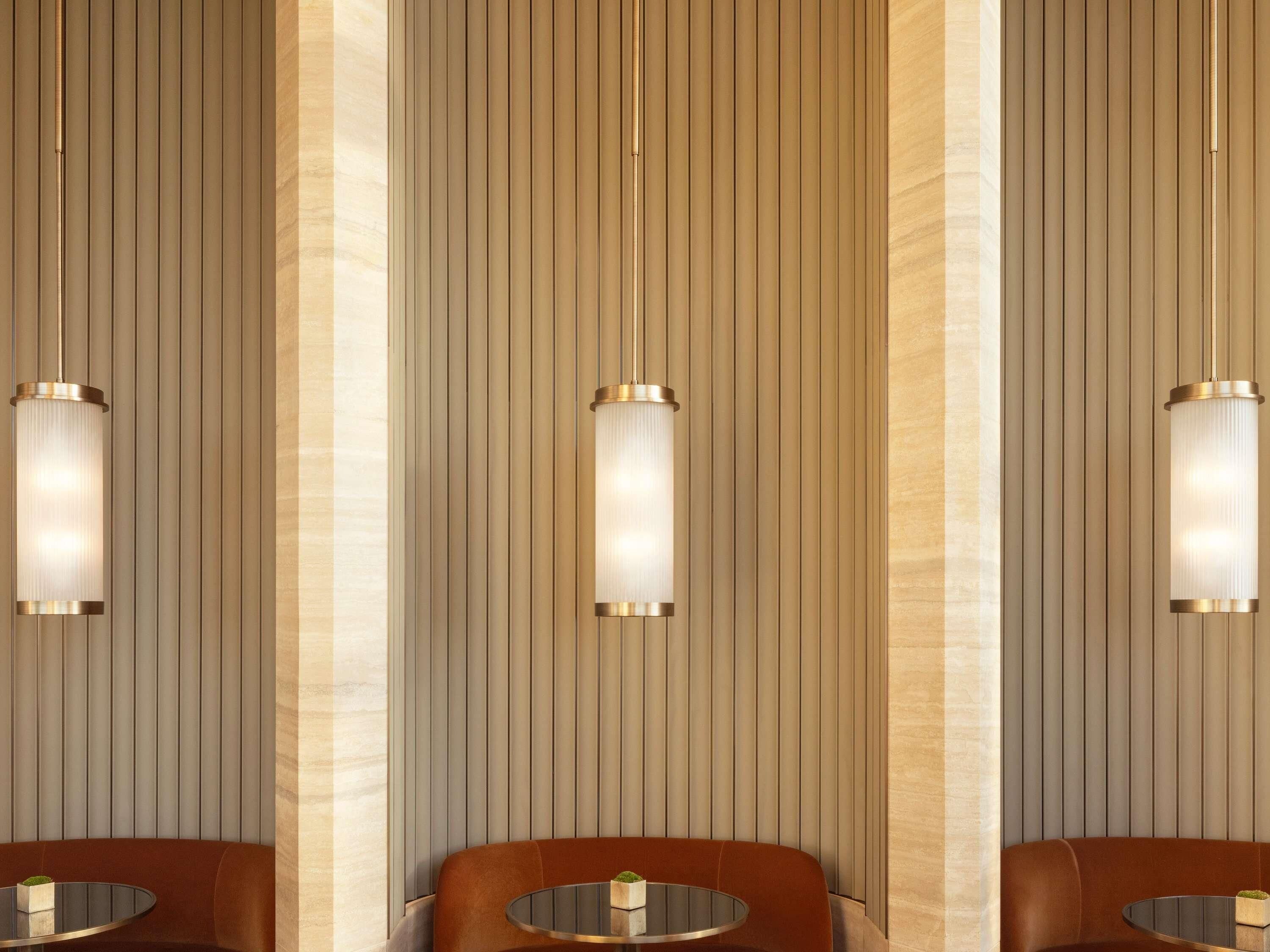 A room with three round tables and chairs, vertical paneling on the walls, and pendant lighting fixtures.