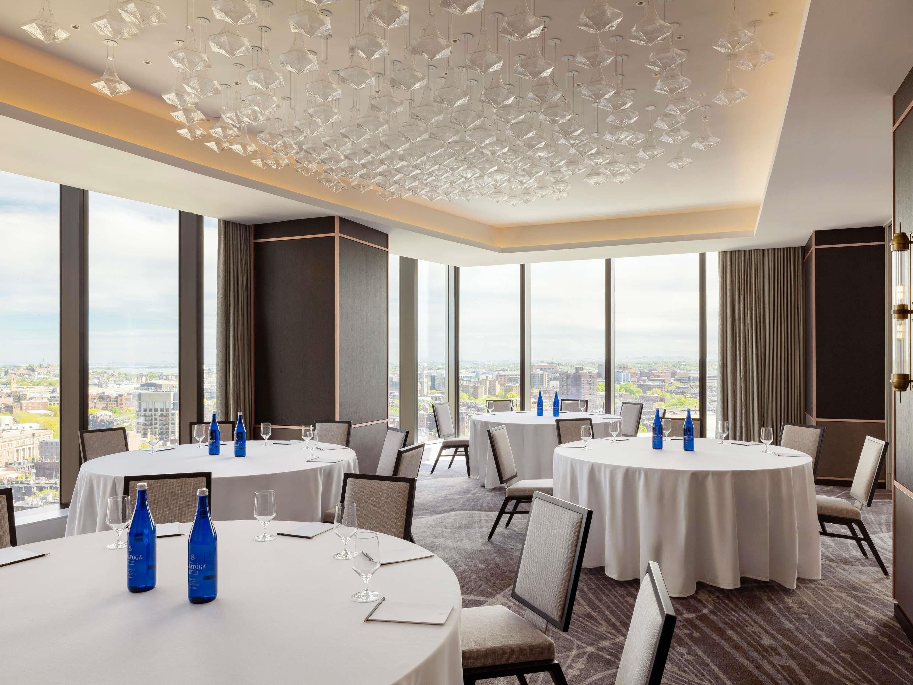 Une salle à manger d’hôtel avec des tables rondes, des chaises et des bouteilles d’eau.