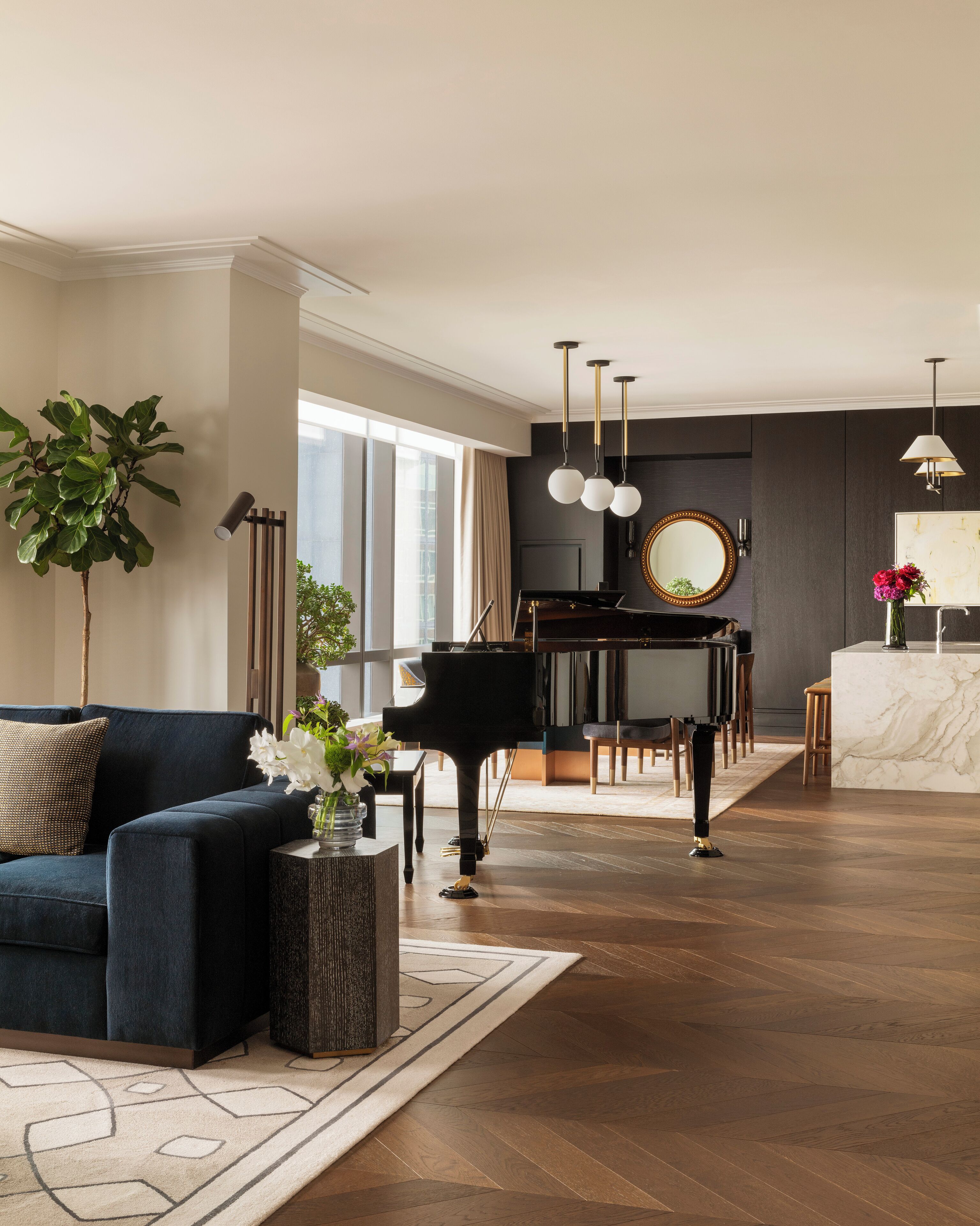 Una sala de estar moderna con un sofá azul oscuro, un piano de cola y una isla de cocina de mármol.