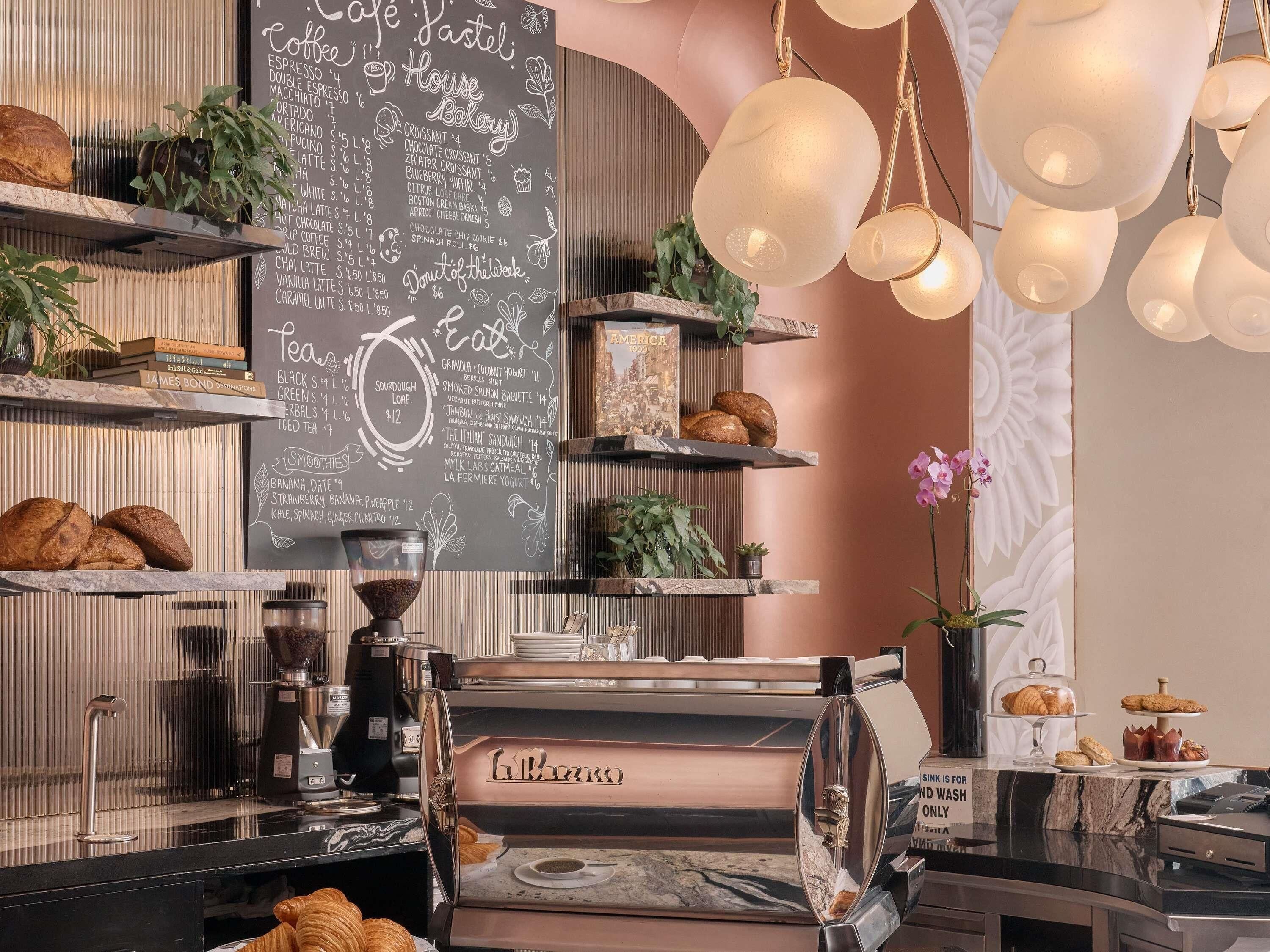 A cafe interior with a chalkboard menu, coffee machine, shelves with baked goods, and hanging pendant lights.