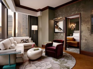 A modern hotel room with a large window, a sofa, a red armchair, a round coffee table, and a bed with a view of the cityscape. - Raffles Boston (Boston)