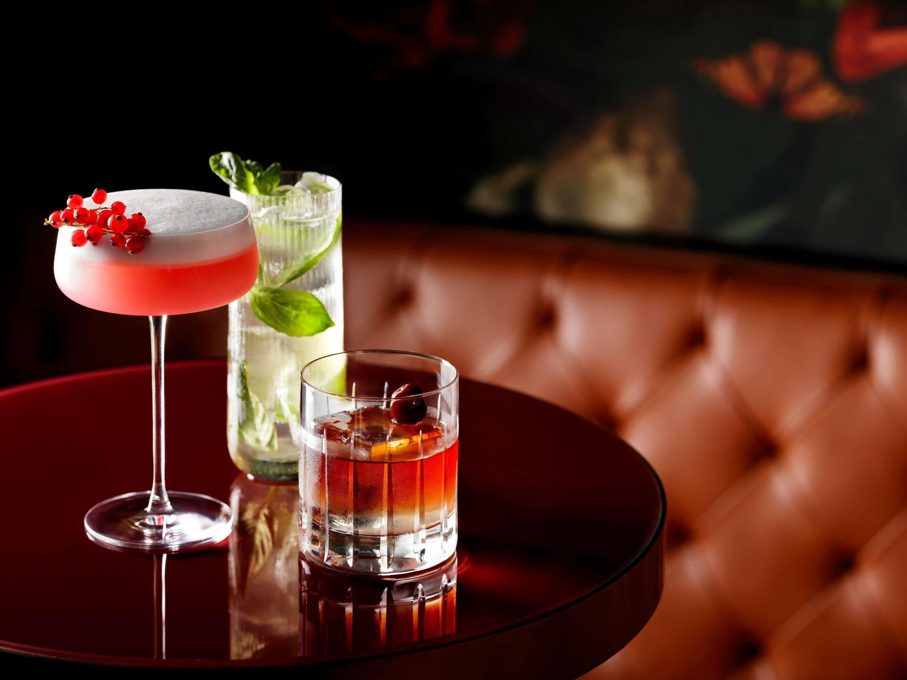 Eine Bar mit einem Cocktail, einem Glas Wasser und einem hohen Glas mit einem Getränk und einer Garnitur.