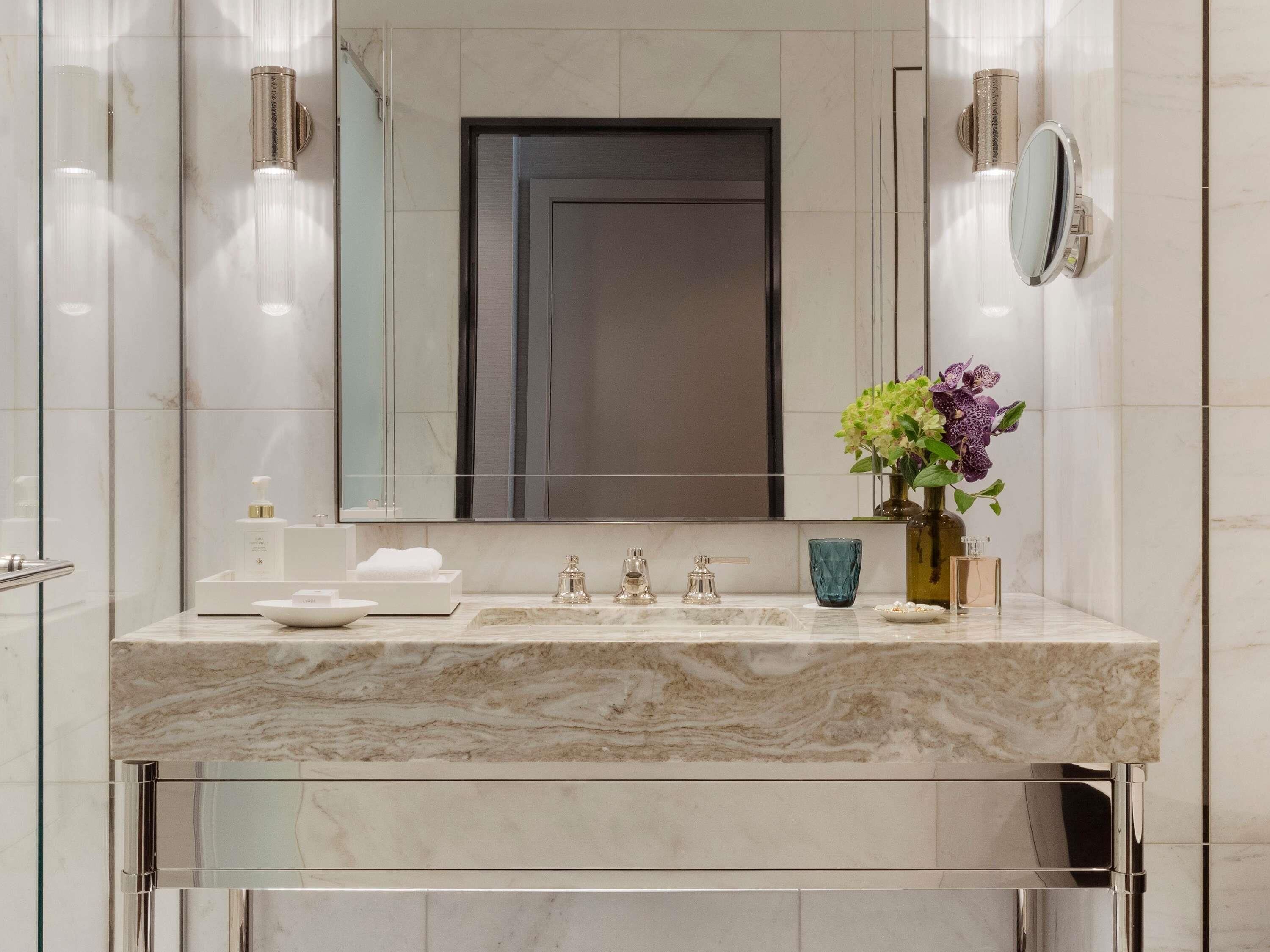 Un baño moderno con un lavamanos de mármol, un espejo grande y un florero con flores.