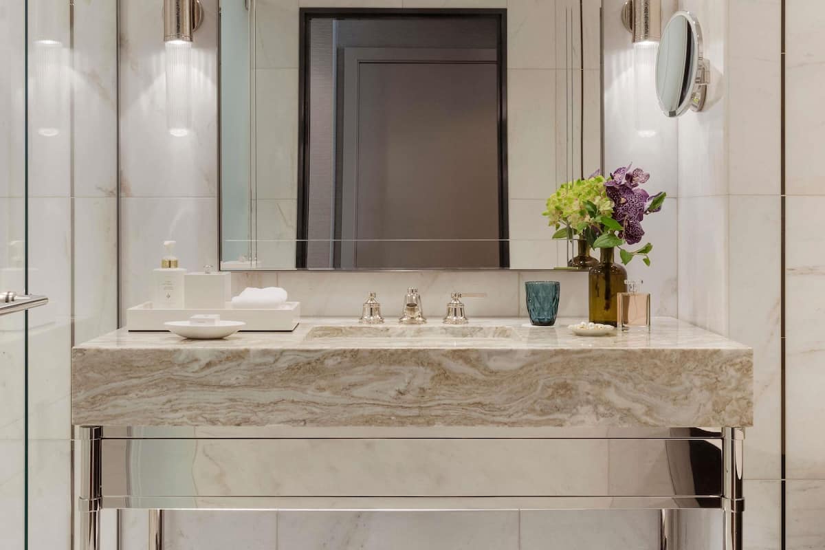 Un baño moderno con un lavamanos de mármol, un espejo grande y un florero con flores.