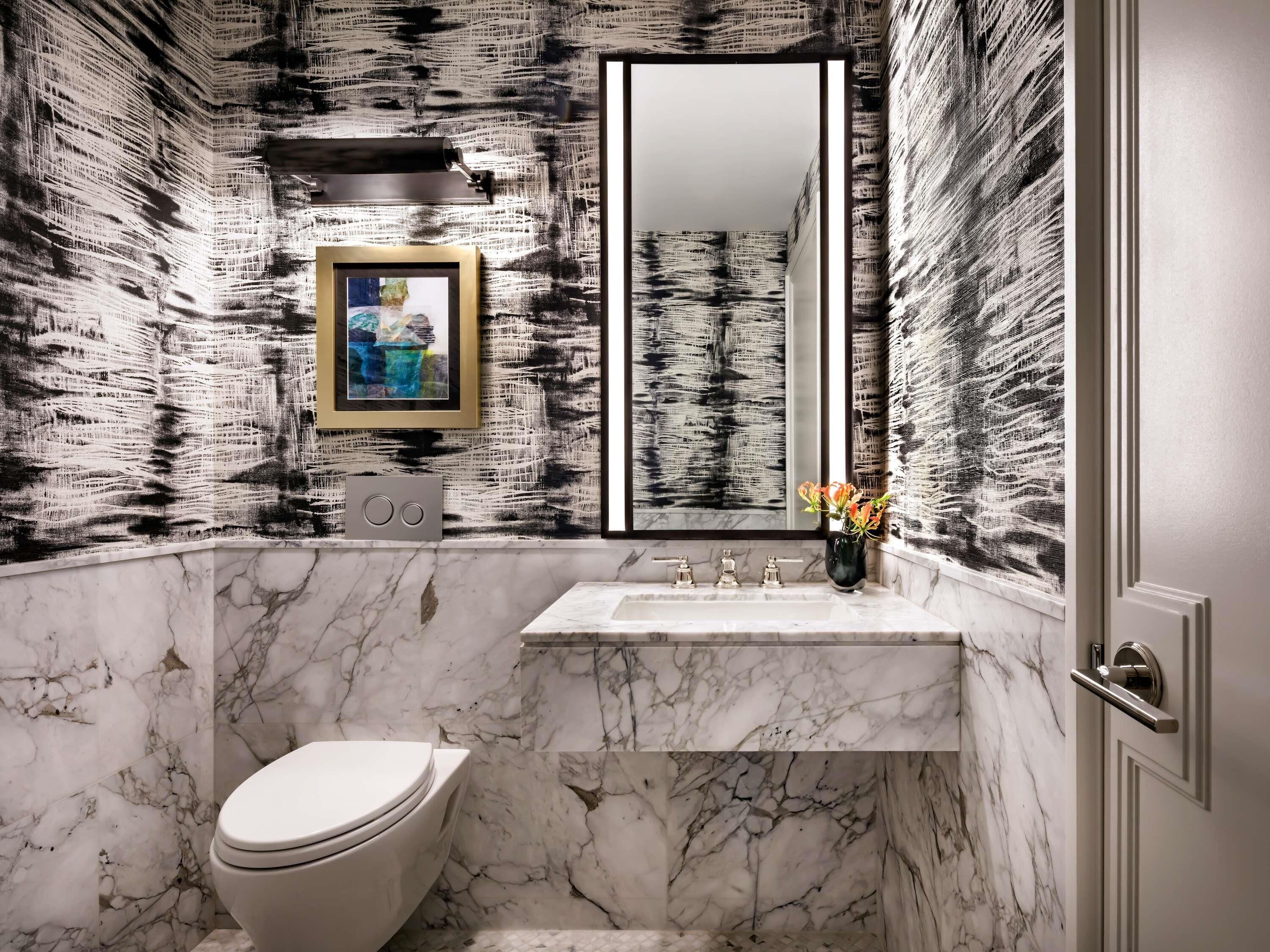 A bathroom with a marble sink, a toilet, a framed picture, and a mirror.
