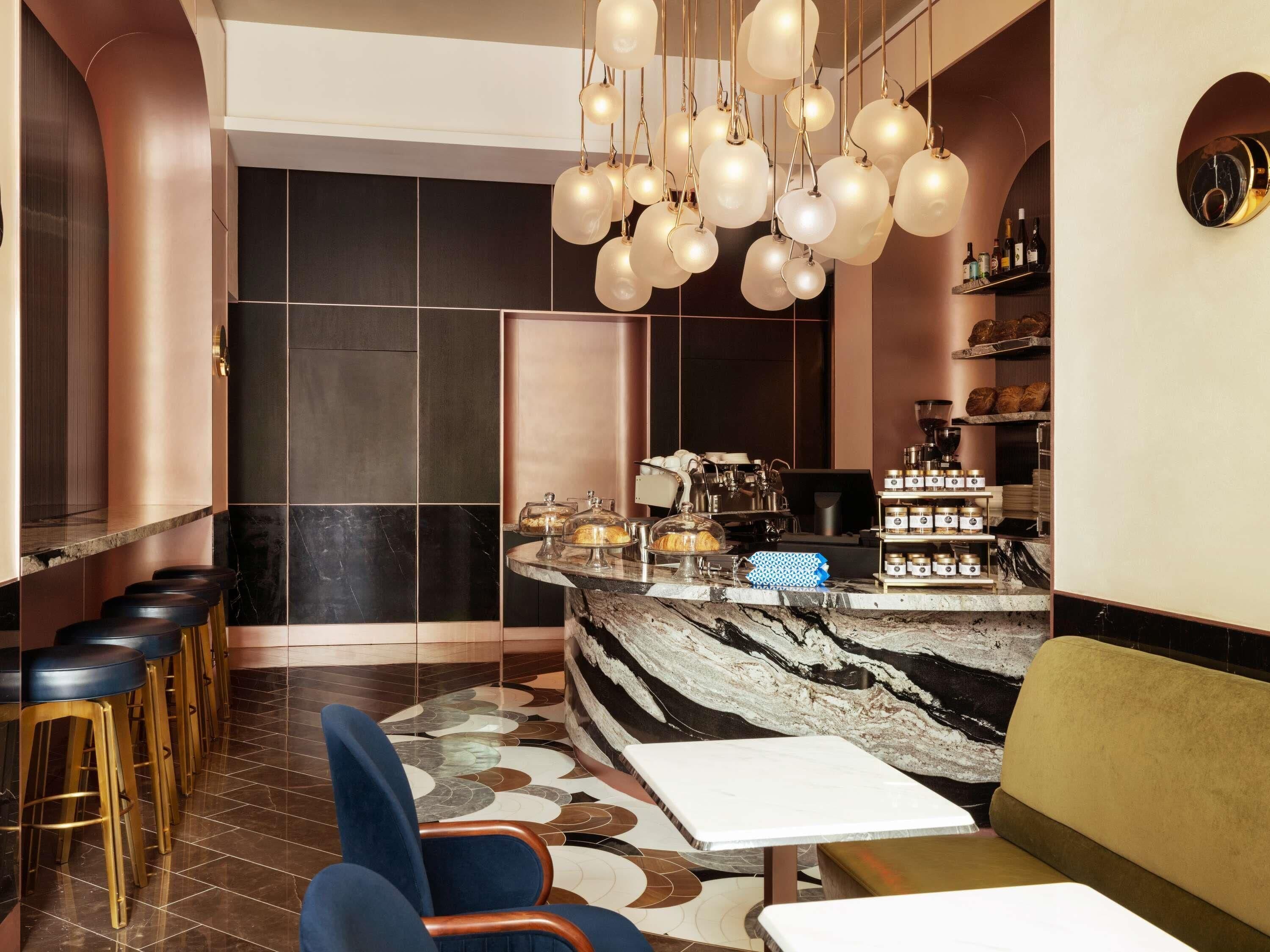 A modern bar area with a marble countertop, stools, and a coffee machine.