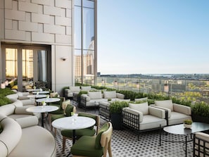 A rooftop terrace with outdoor seating, a view of the city, and a modern building facade. - Raffles Boston (Boston)
