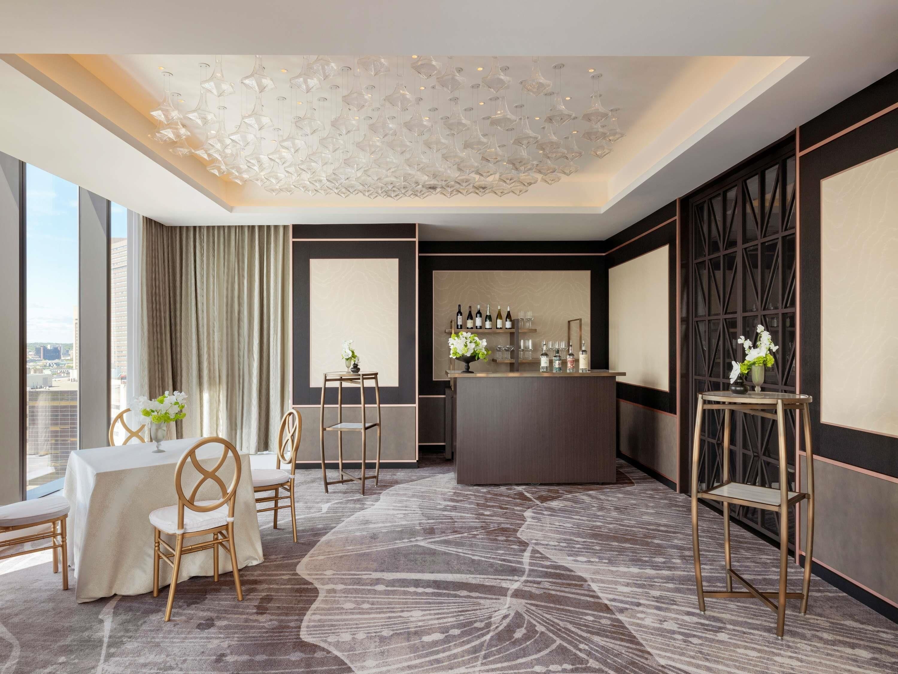 Une chambre d’hôtel dotée d’un coin repas, d’un bar et d’une grande fenêtre donnant sur la ville.