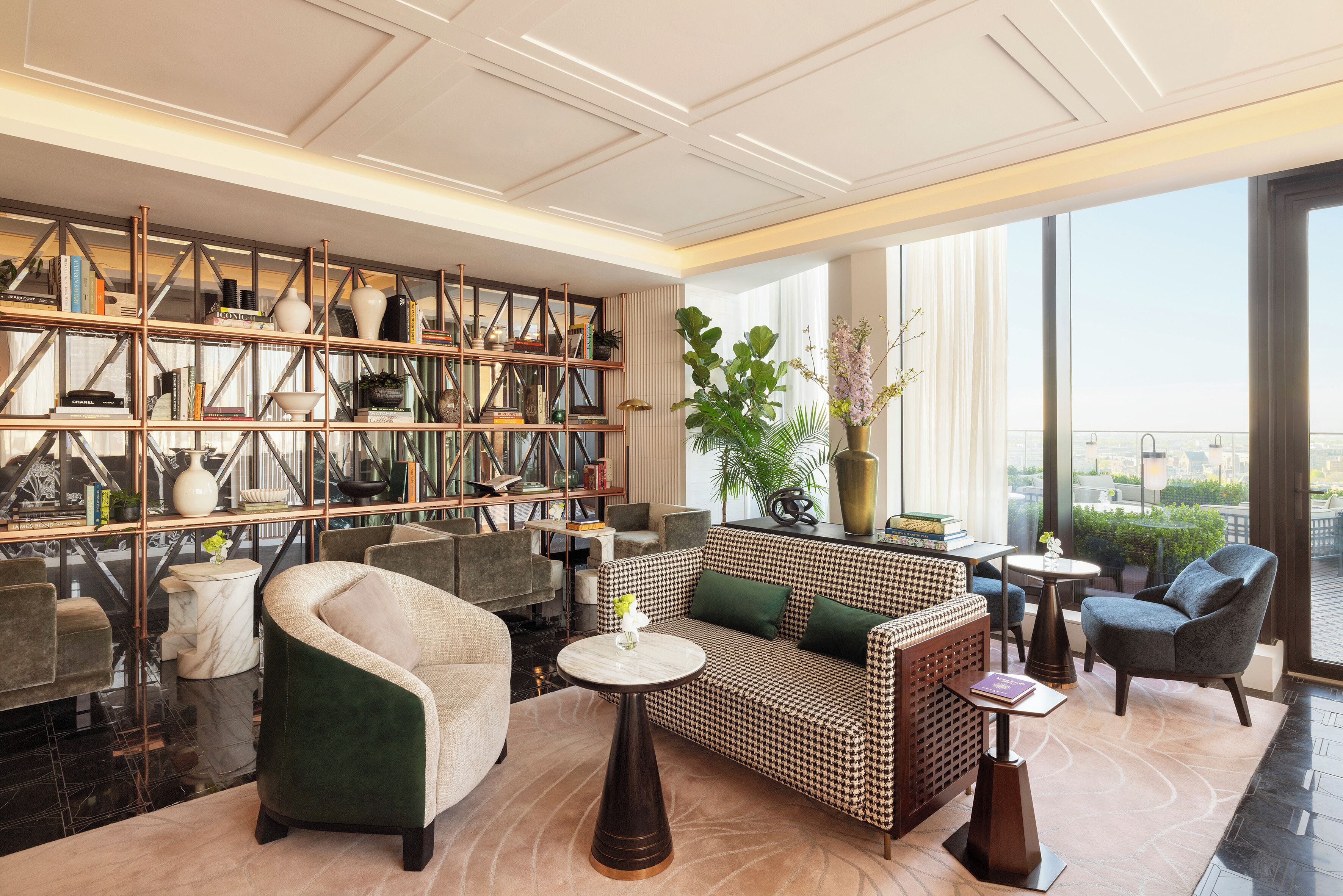Ein stilvoller Lounge-Bereich mit einem gemusterten Sofa, Sesseln, einem Marmortisch und einer großen Bücherwand voller Bücher und Dekoration.