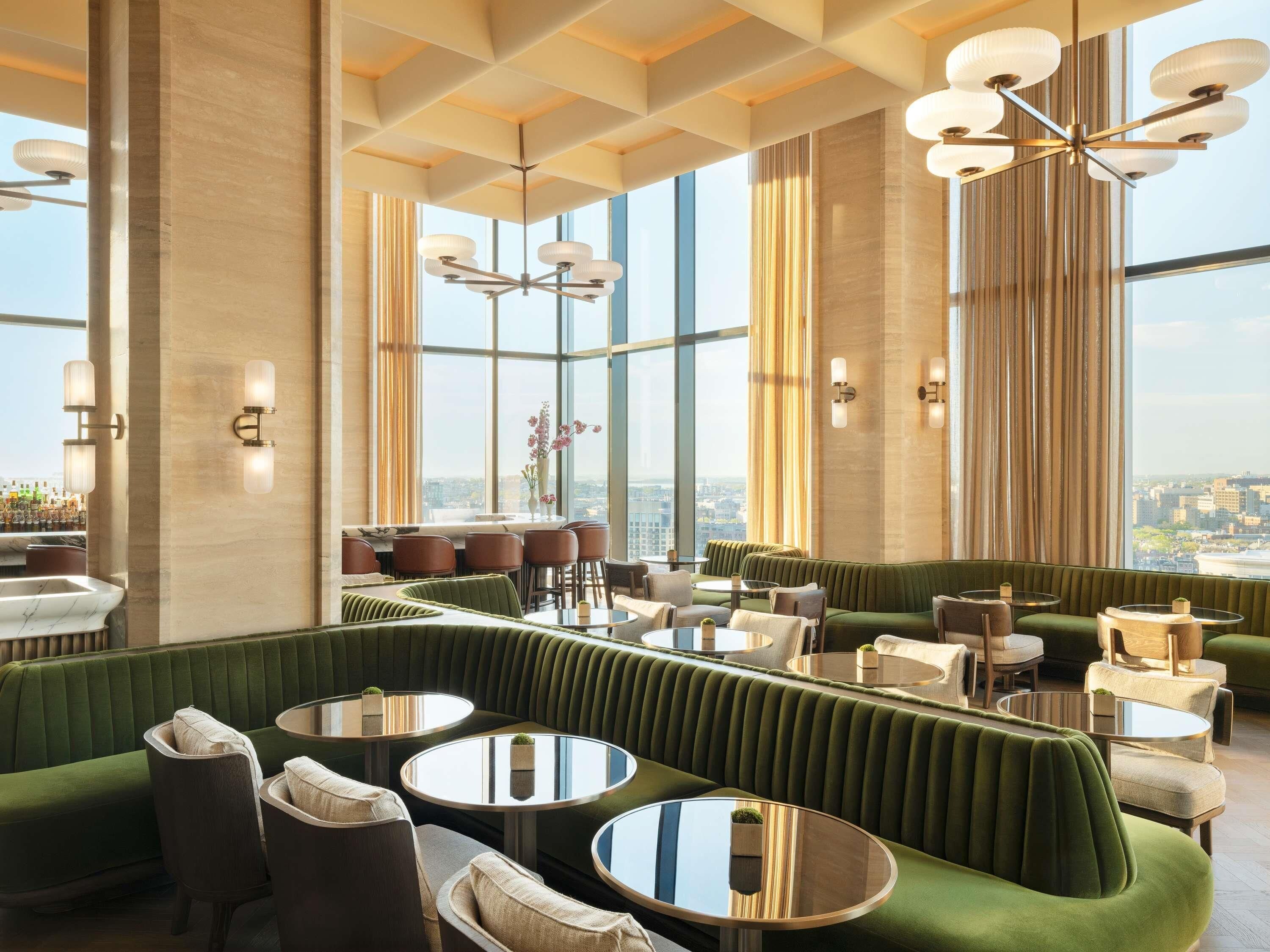 A modern interior with a green upholstered seating area, round tables, and a city view.