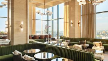 A modern interior with a green upholstered seating area, round tables, and a city view.