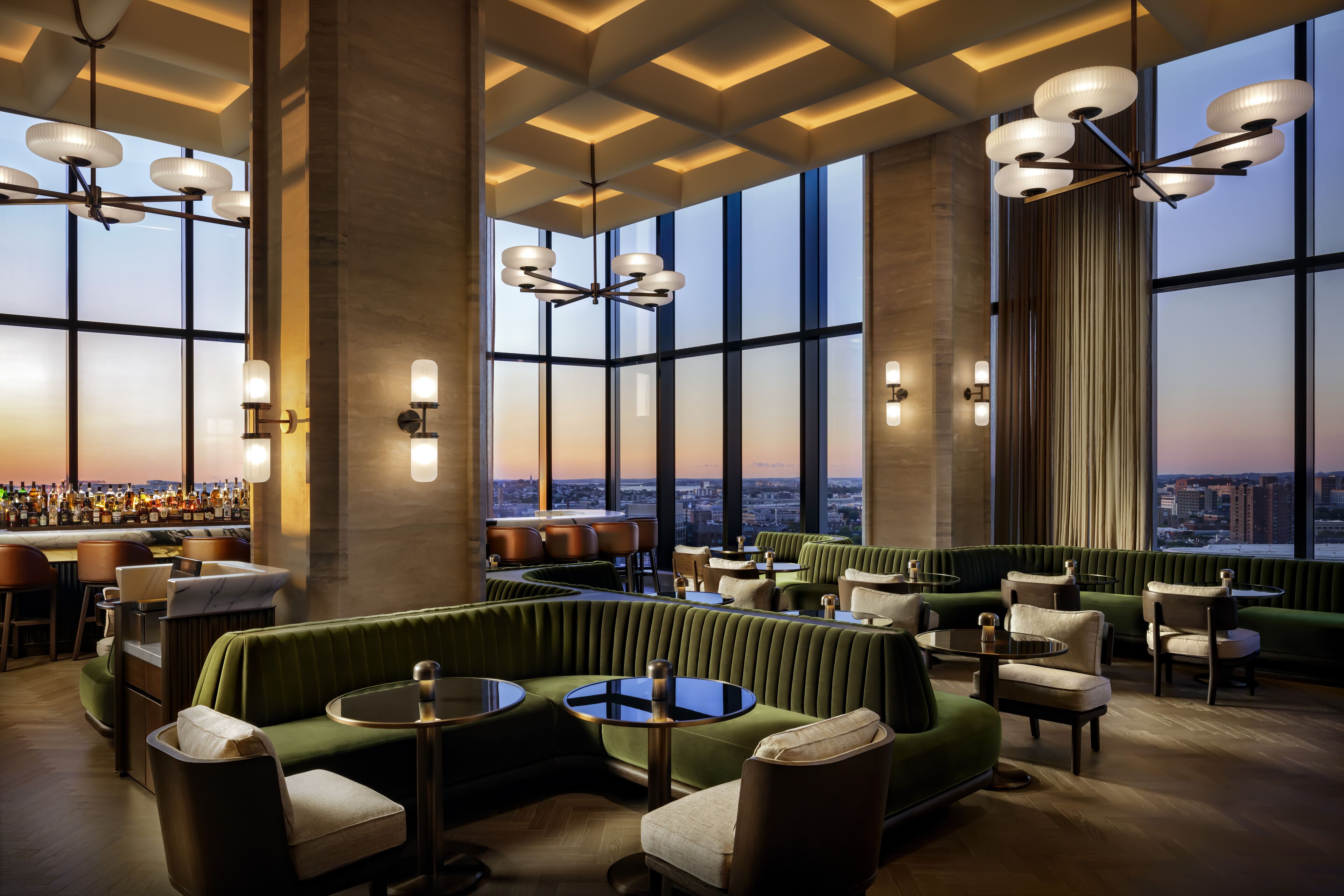 A modern bar/lounge area with green seating, large windows, and city views.