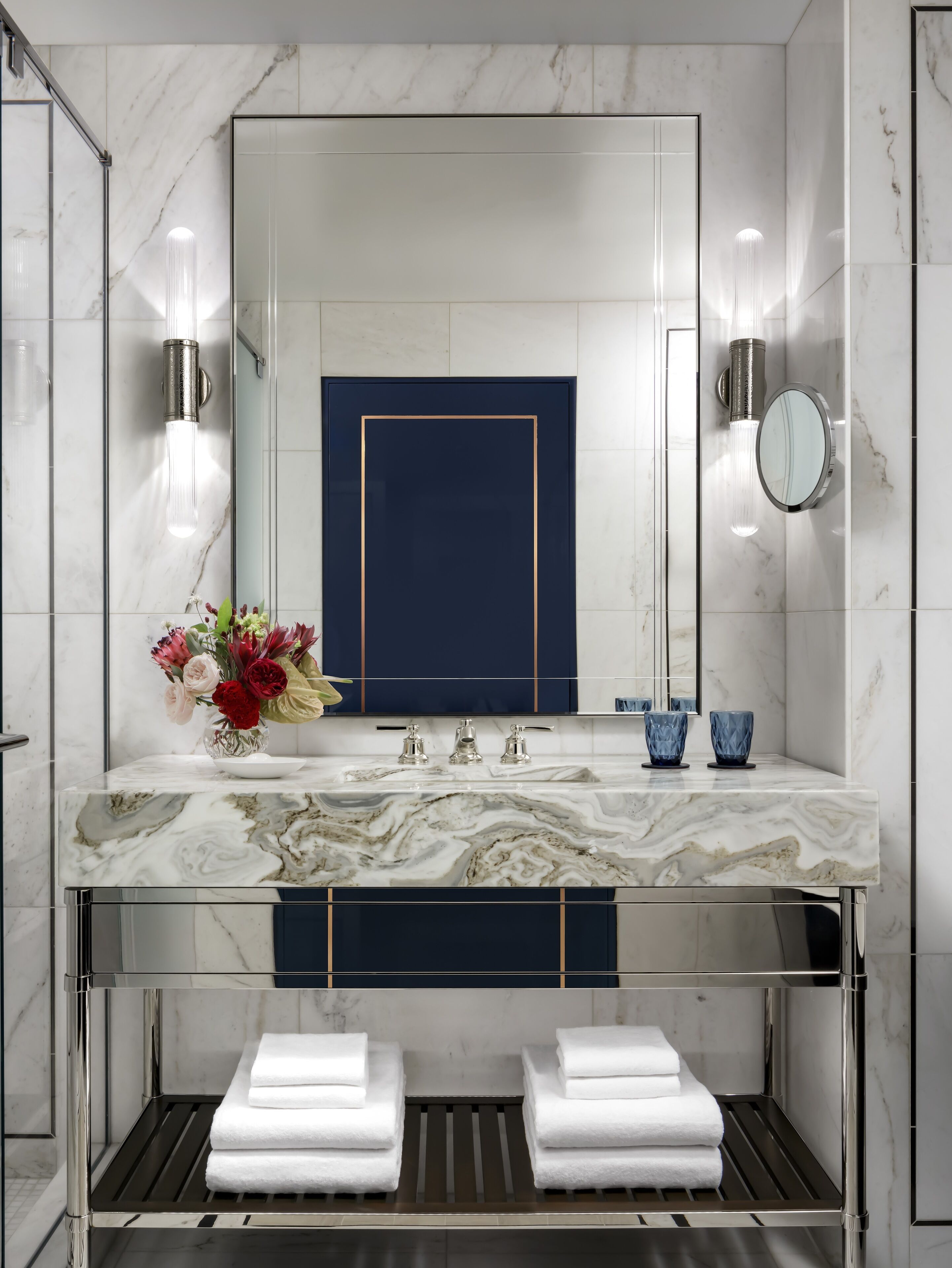 A modern bathroom with a marble vanity, a large mirror, a blue accent wall, and a towel rack.