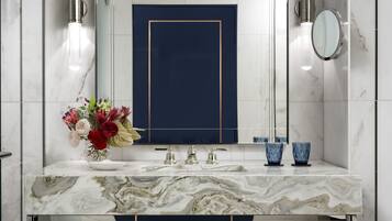 A modern bathroom with a marble vanity, a large mirror, a blue accent wall, and a towel rack.