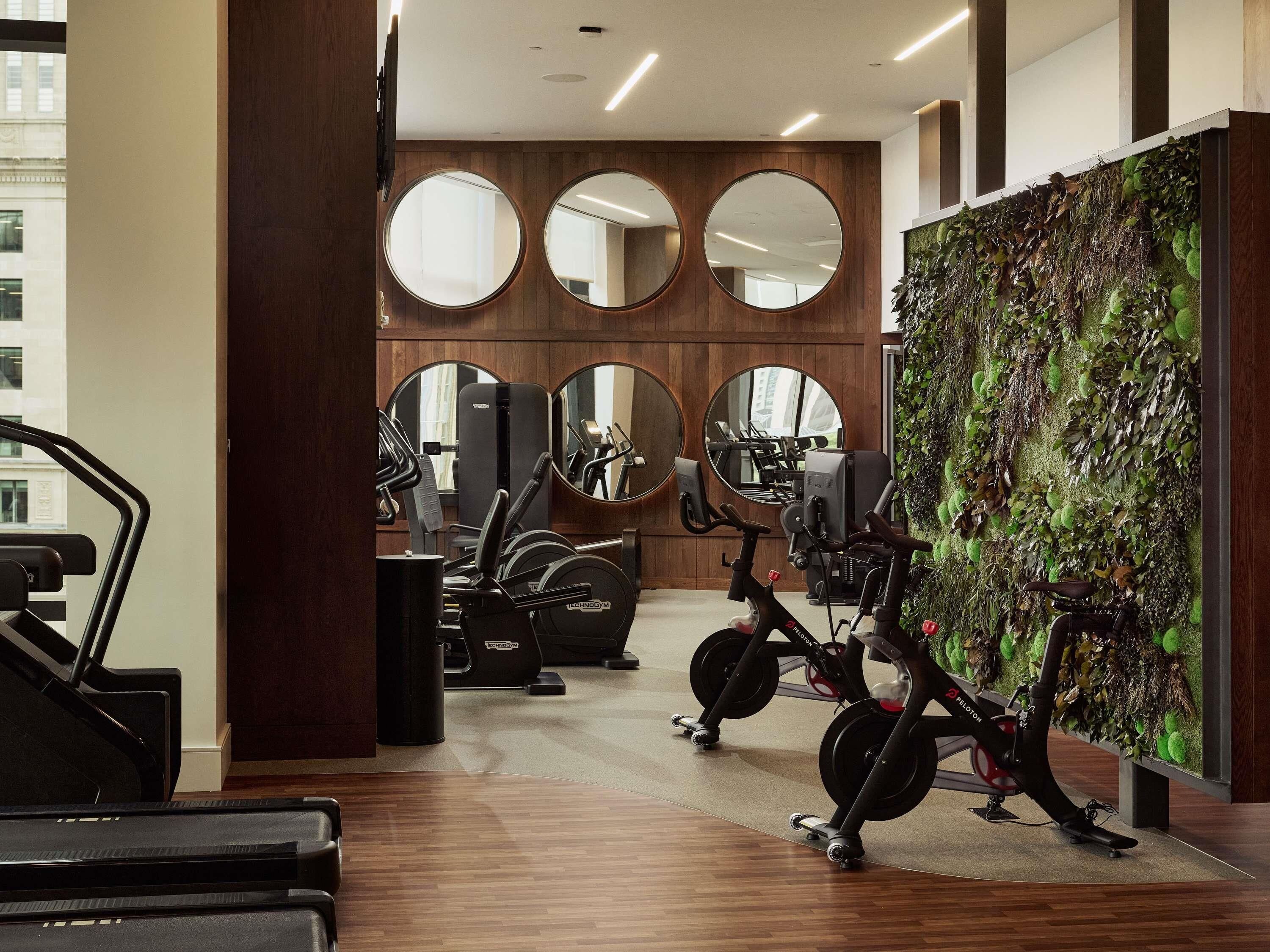 Une salle de sport équipée de matériel d’exercice, de miroirs et d’un mur végétal.