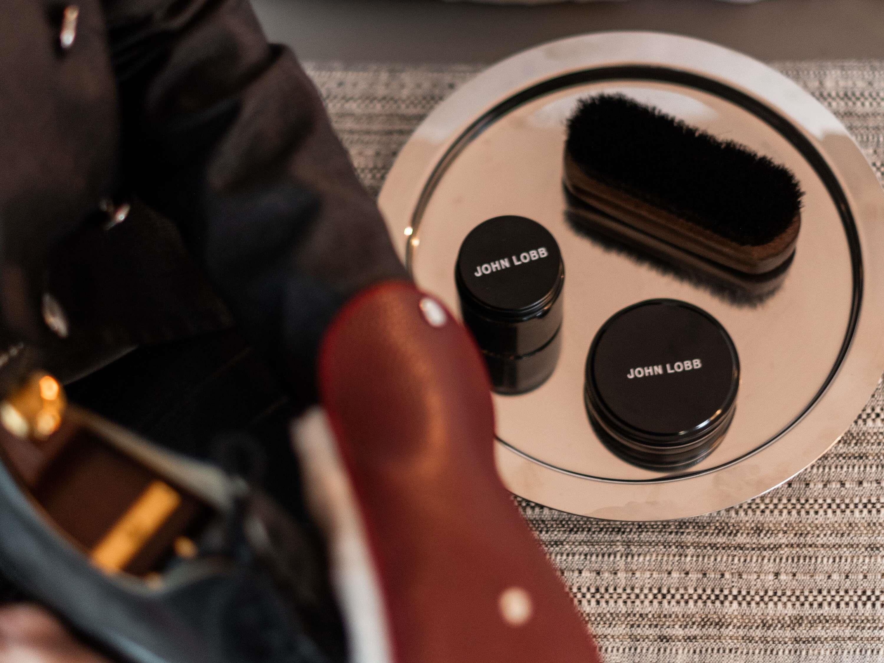 A round tray with two black containers labeled 'JOHN LOBB' and a black brush.