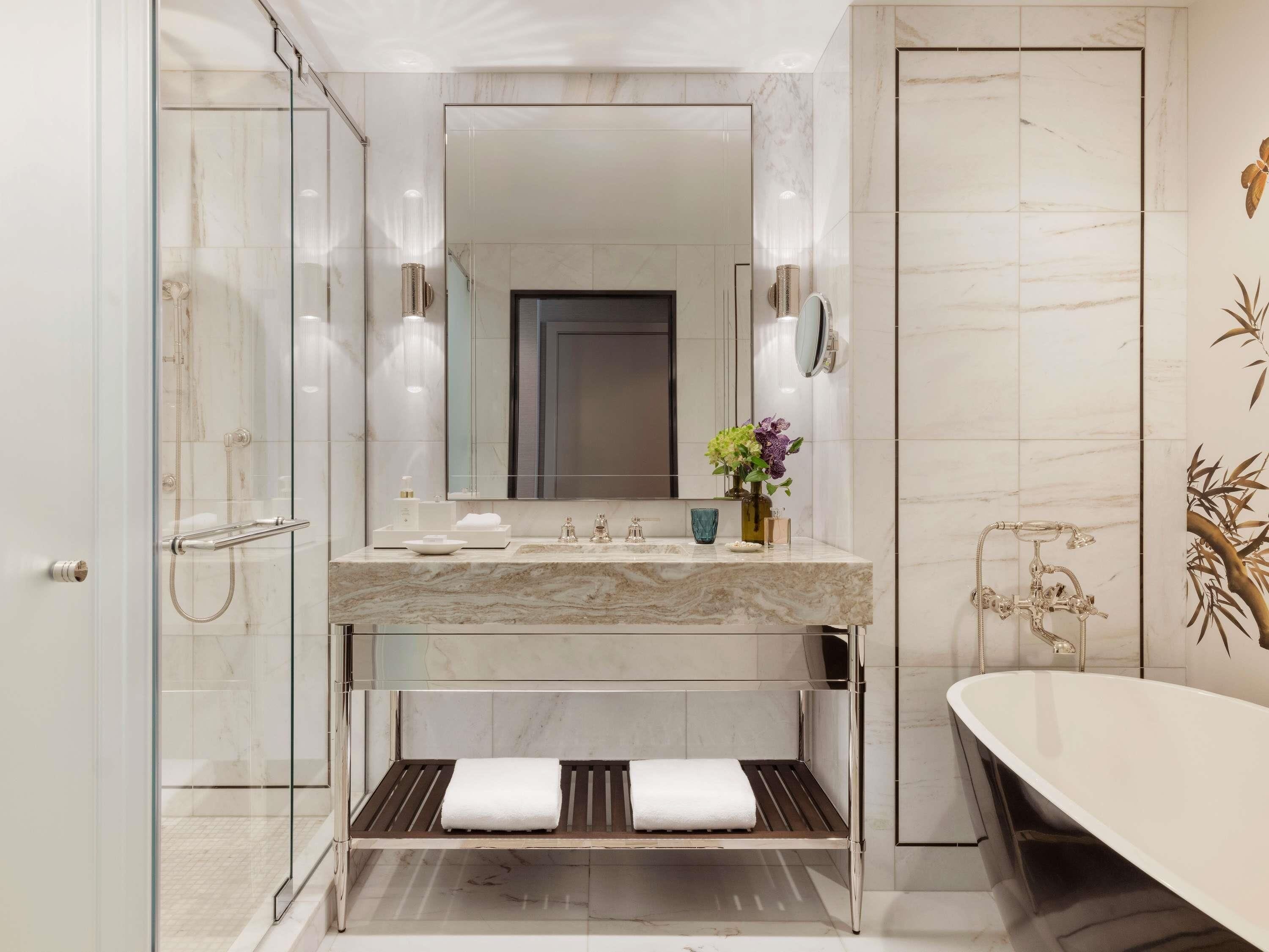 A modern bathroom with a glass-enclosed shower, a marble vanity, and a freestanding bathtub.