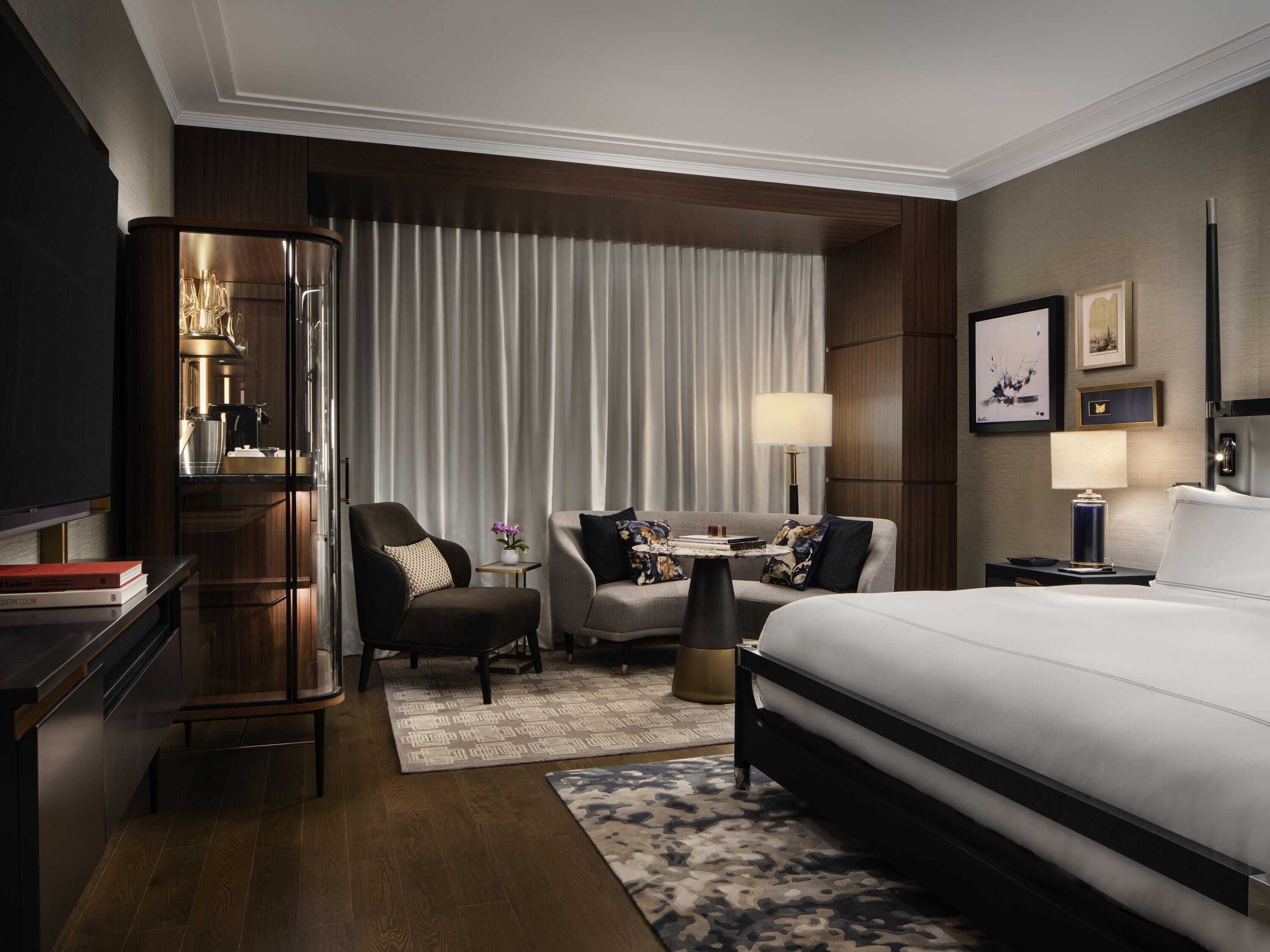 A hotel room with a bed, a desk, a chair, a sofa, a TV, and a lamp.