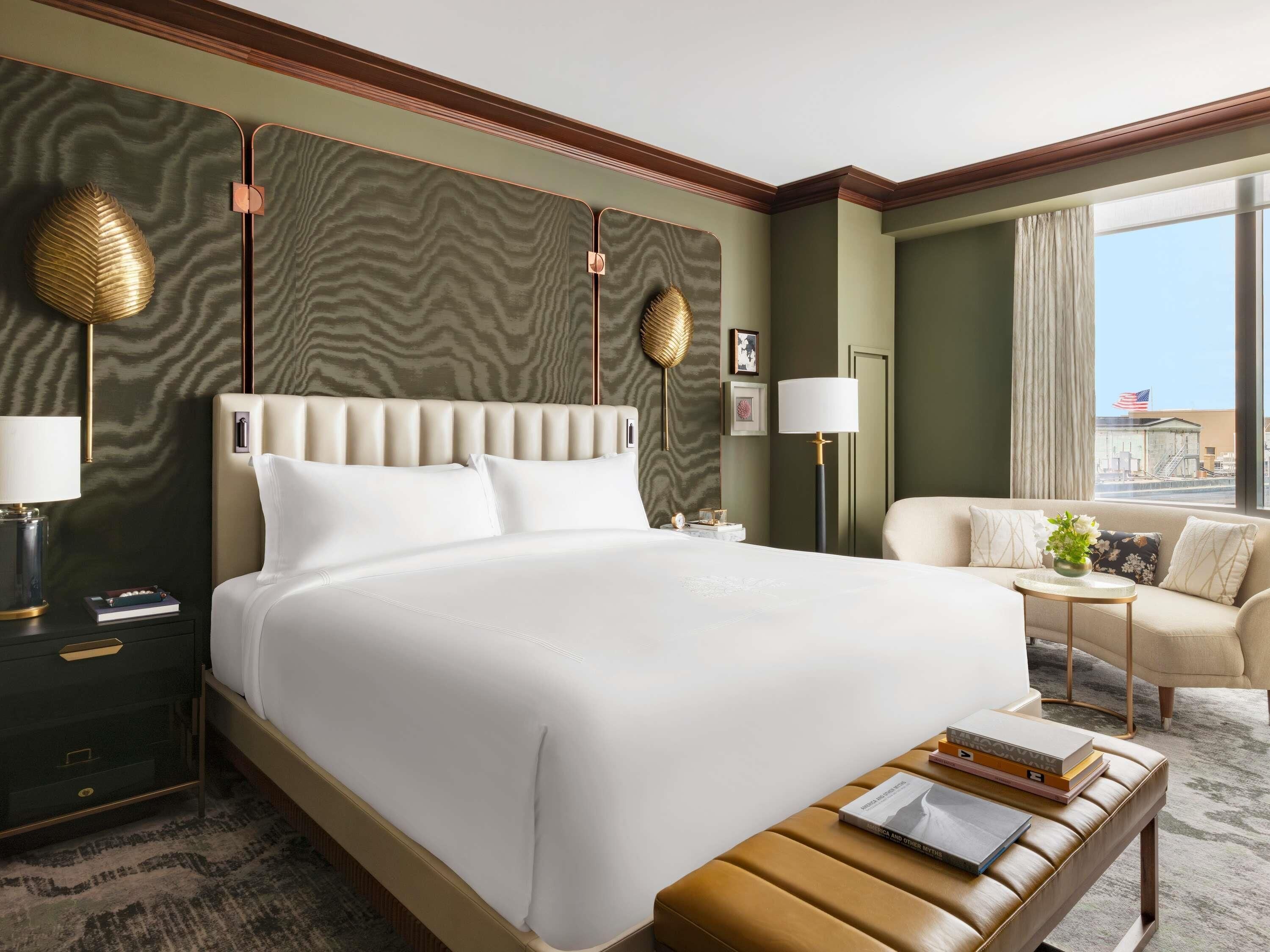 A hotel room with a large bed, a sofa, a small table, and a view of the city.
