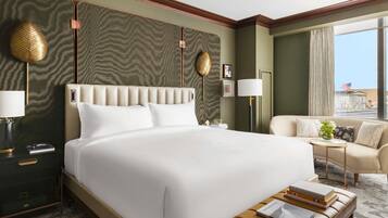 A hotel room with a large bed, a sofa, a small table, and a view of the city.