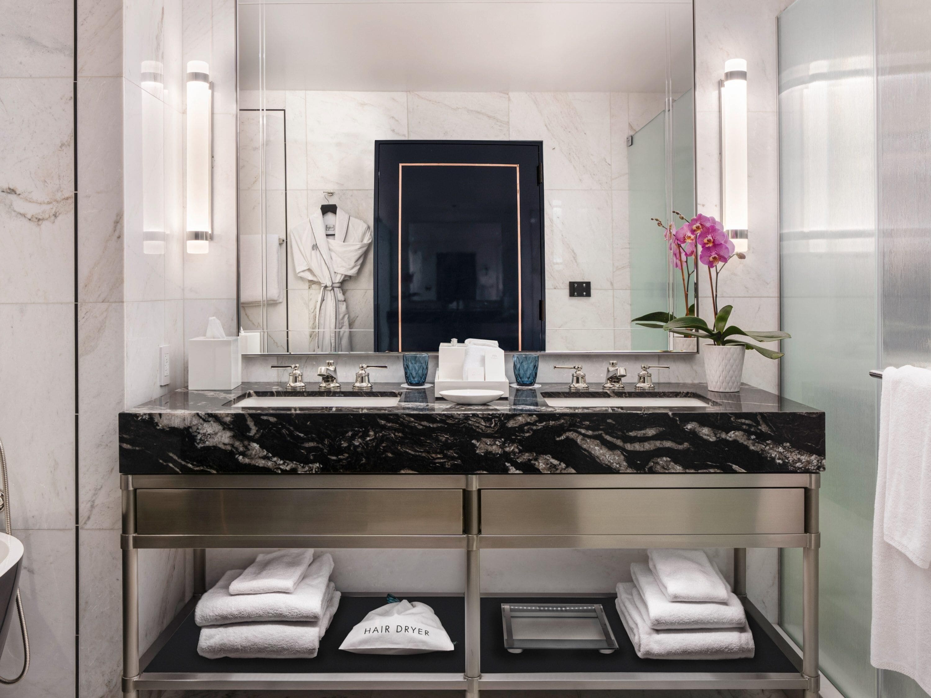 A modern bathroom with a marble sink, a large mirror, a robe, and a hair dryer.