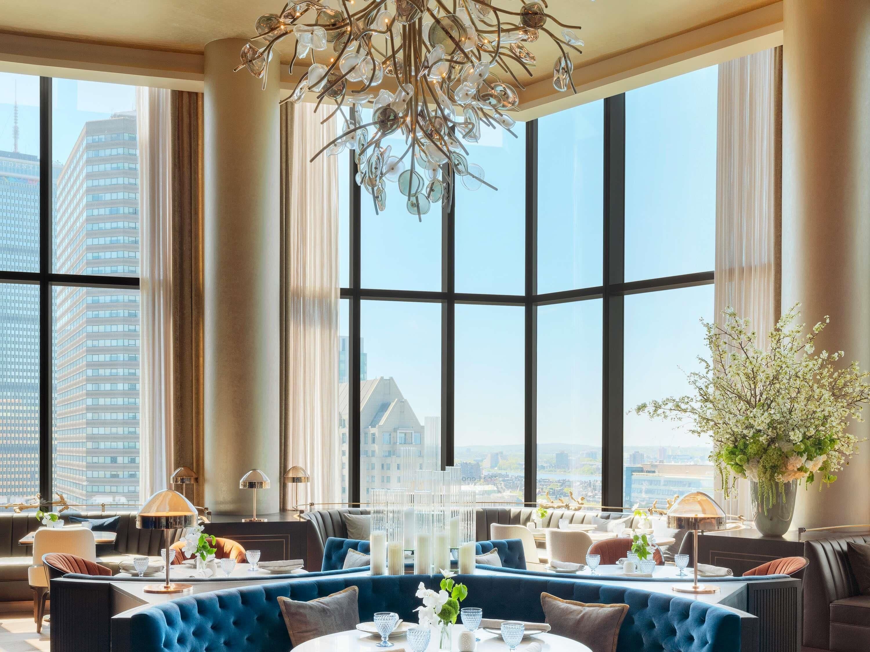 A modern dining area with large windows, a chandelier, and a view of the cityscape.