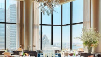 A modern dining area with large windows, a chandelier, and a view of the cityscape.