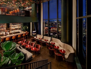 A bar area with a city view, seating with red accents, and a plant.