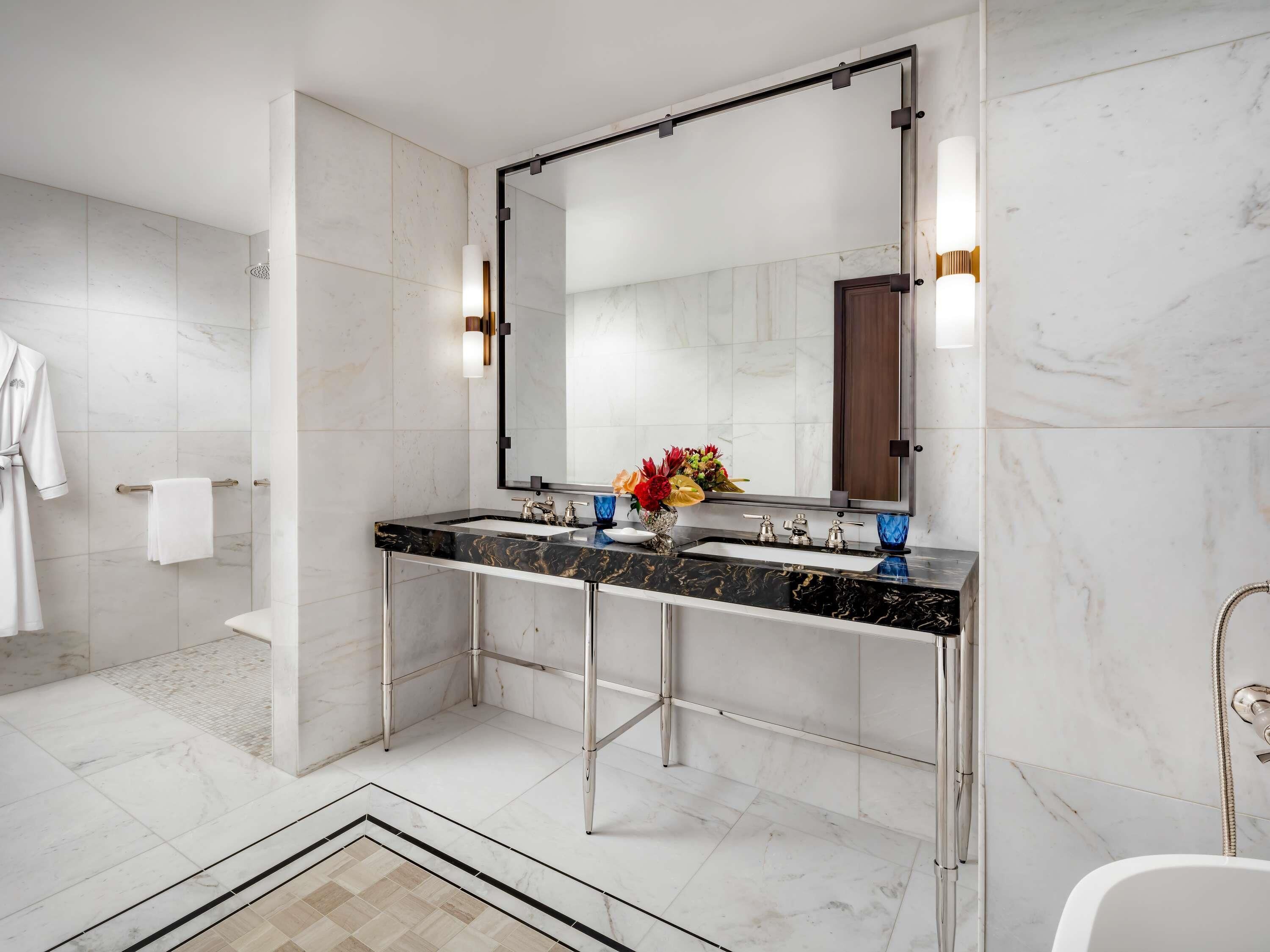 A modern bathroom with a large mirror, a black marble countertop, and a white bathtub.