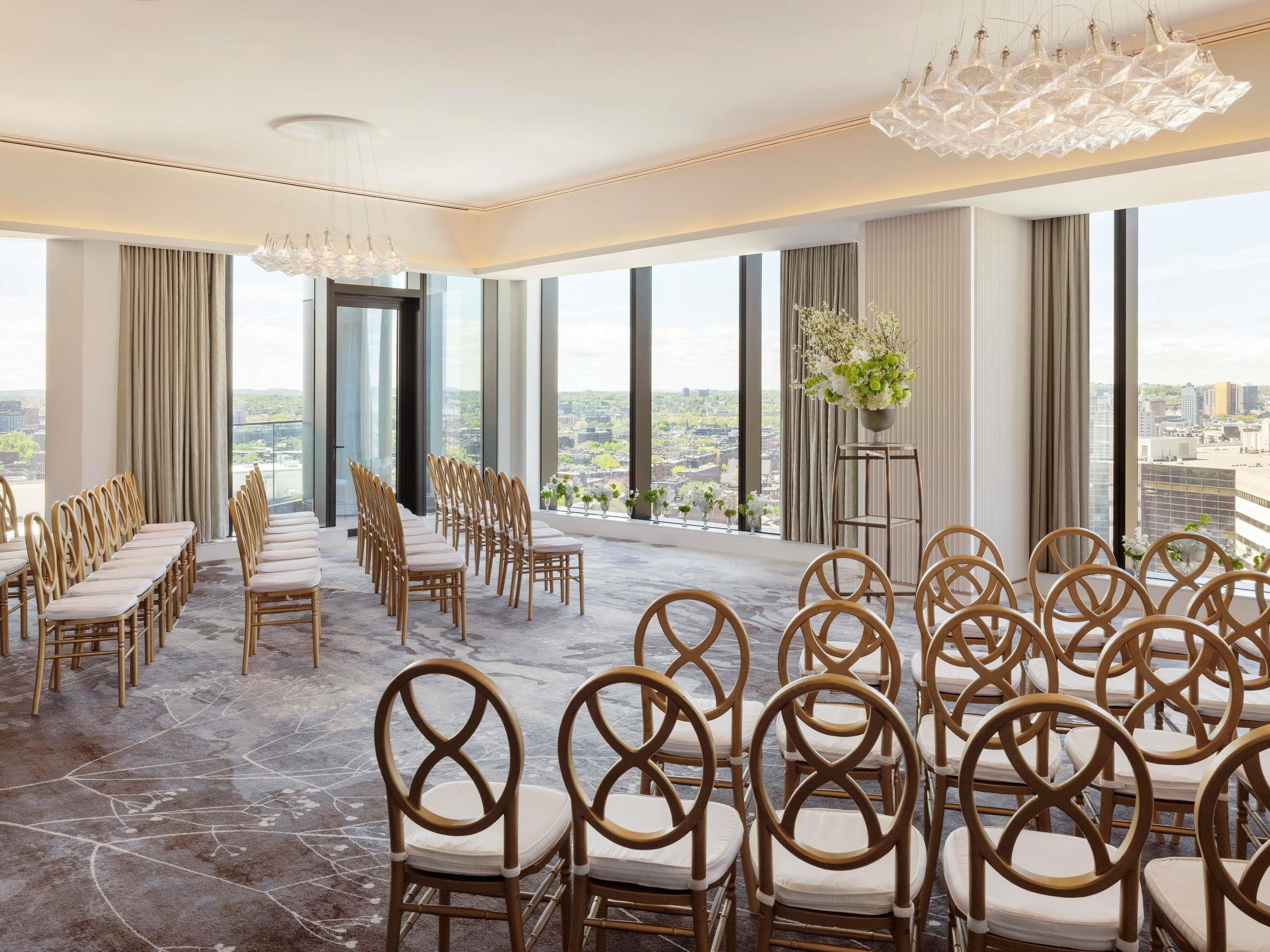 A conference room with rows of chairs and tables, large windows with a city view, and decorative lighting fixtures.