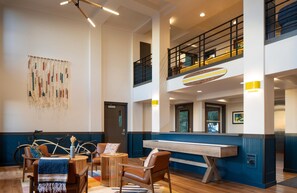 A spacious lobby with a high ceiling, a central seating area with a wooden table, and a bicycle leaning against the wall.