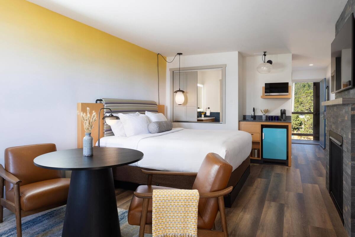 A modern hotel room with a large bed, a small desk, a seating area, and a fireplace.