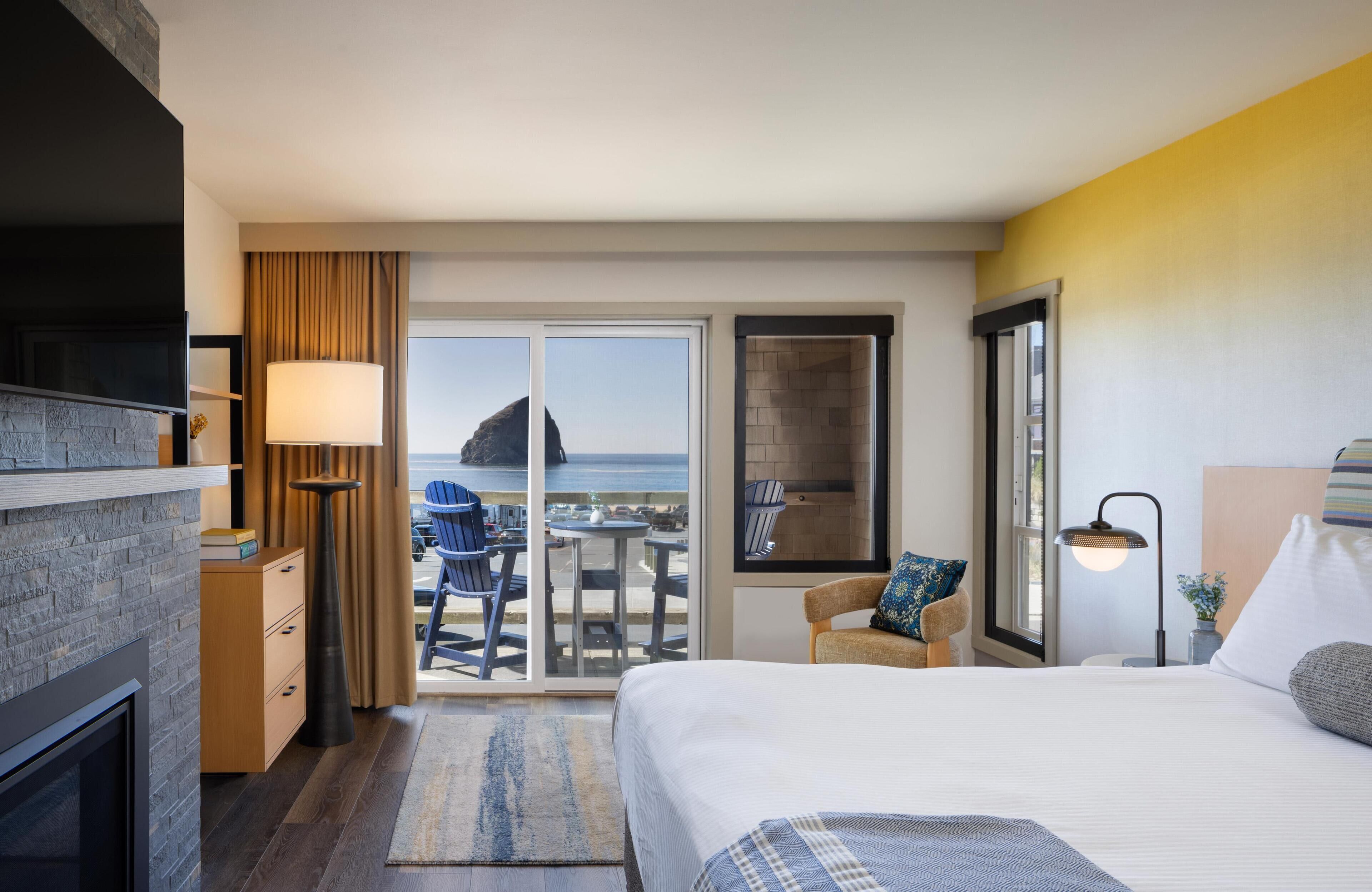A hotel room with a bed, a desk, a chair, a lamp, and a view of the ocean.