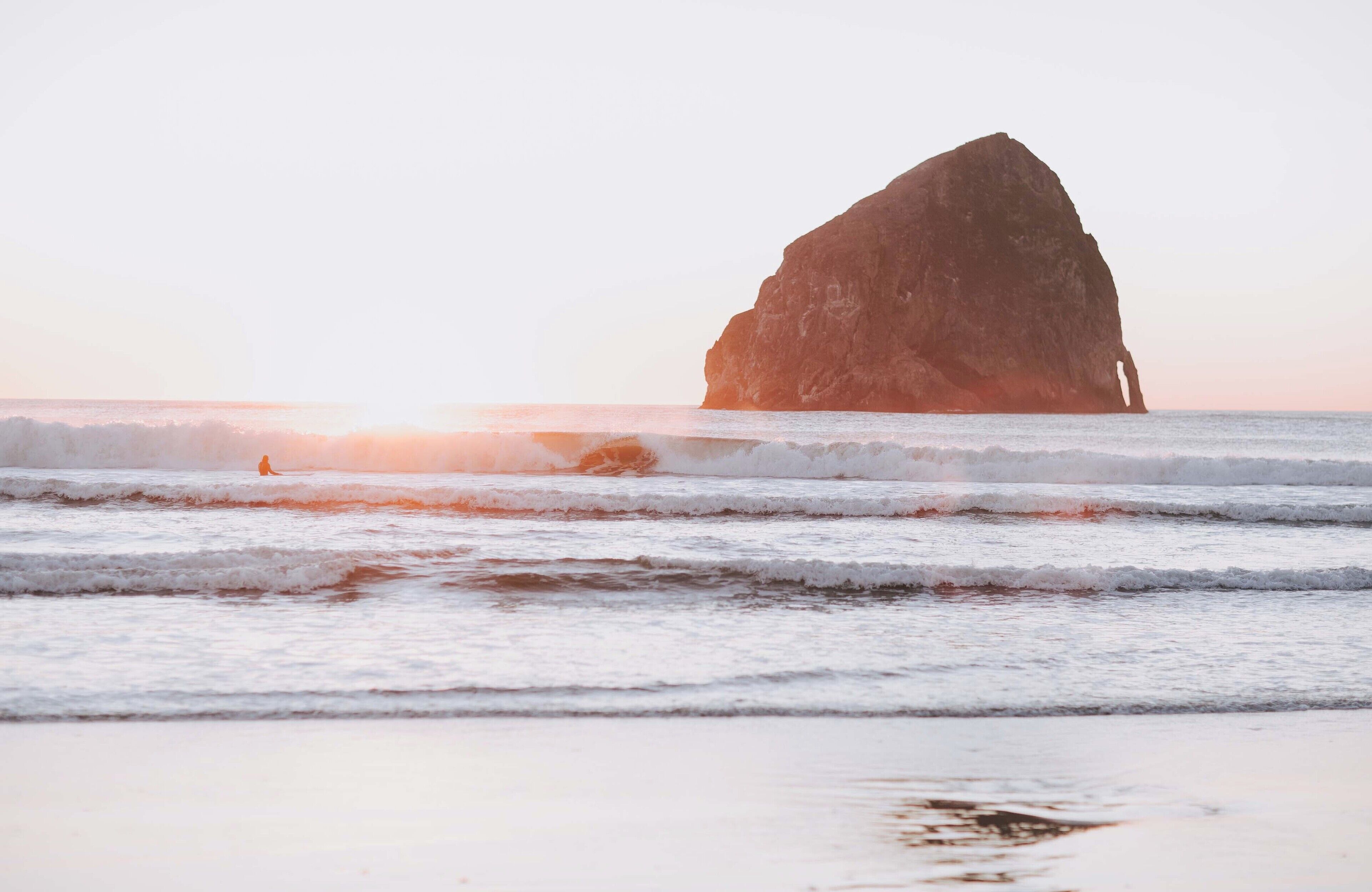 A large rock formation in the ocean with waves crashing against it.