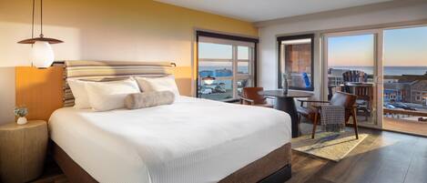 A modern hotel room with a large bed, a desk, and a view of the city.