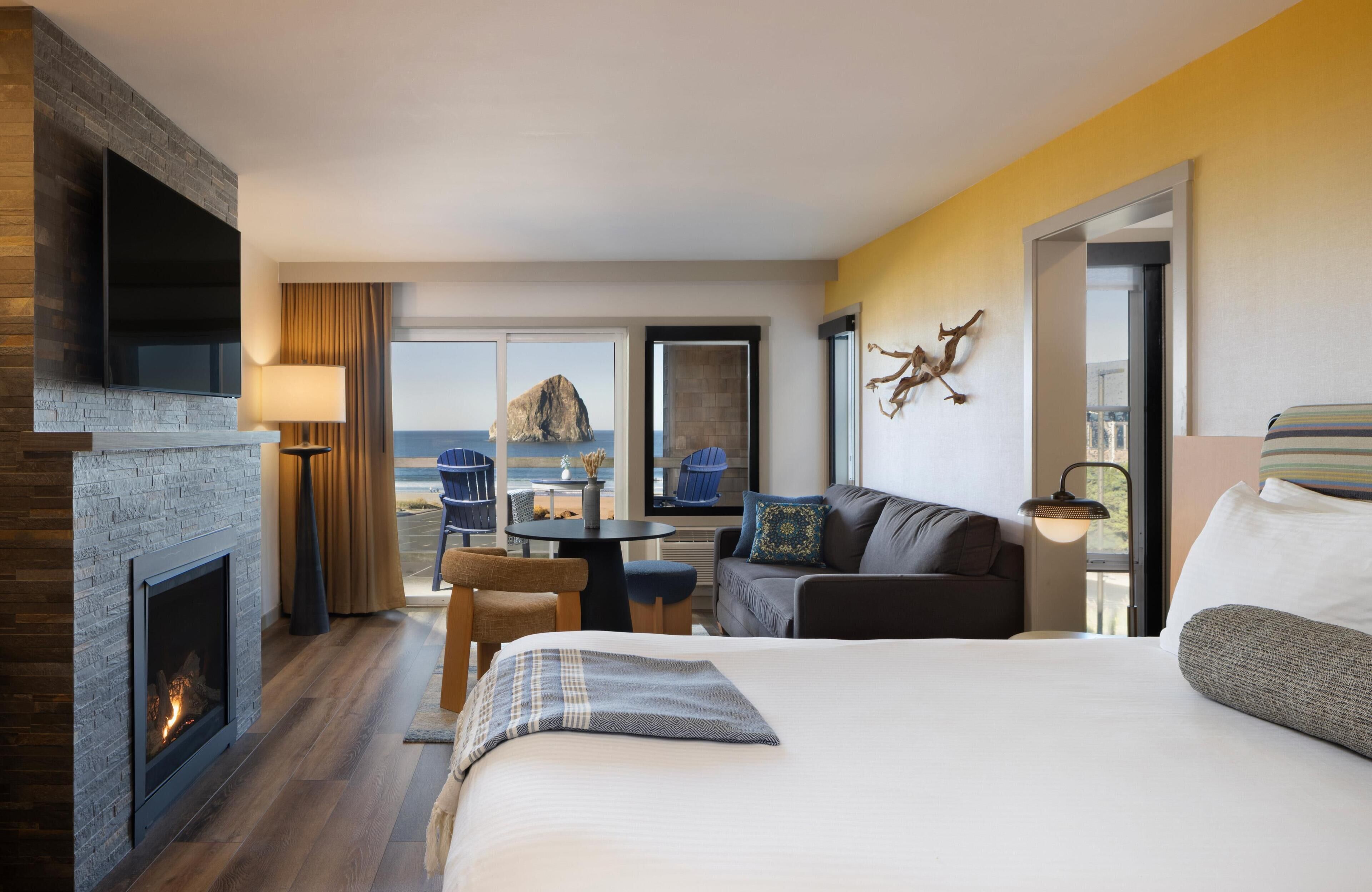 A hotel room with a fireplace, a bed, a sofa, a dining table, and a view of the ocean.