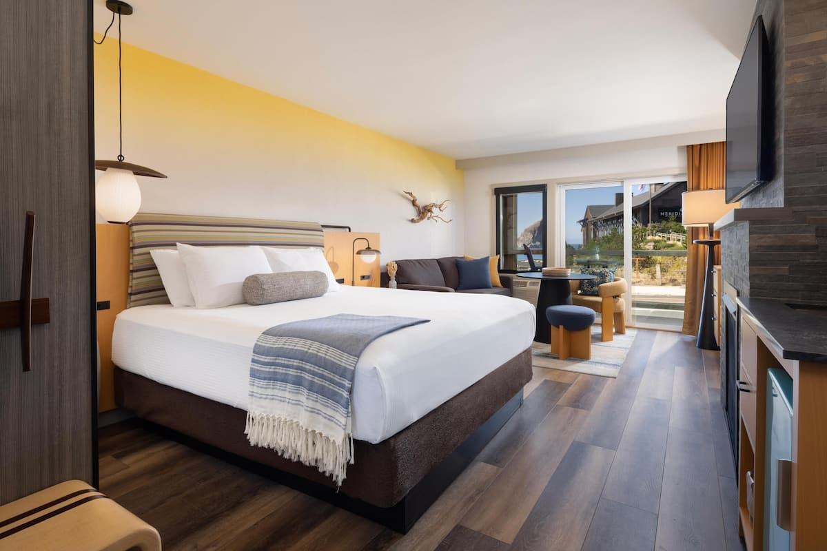 A modern hotel room with a large bed, a sofa, a dining table, and a TV.