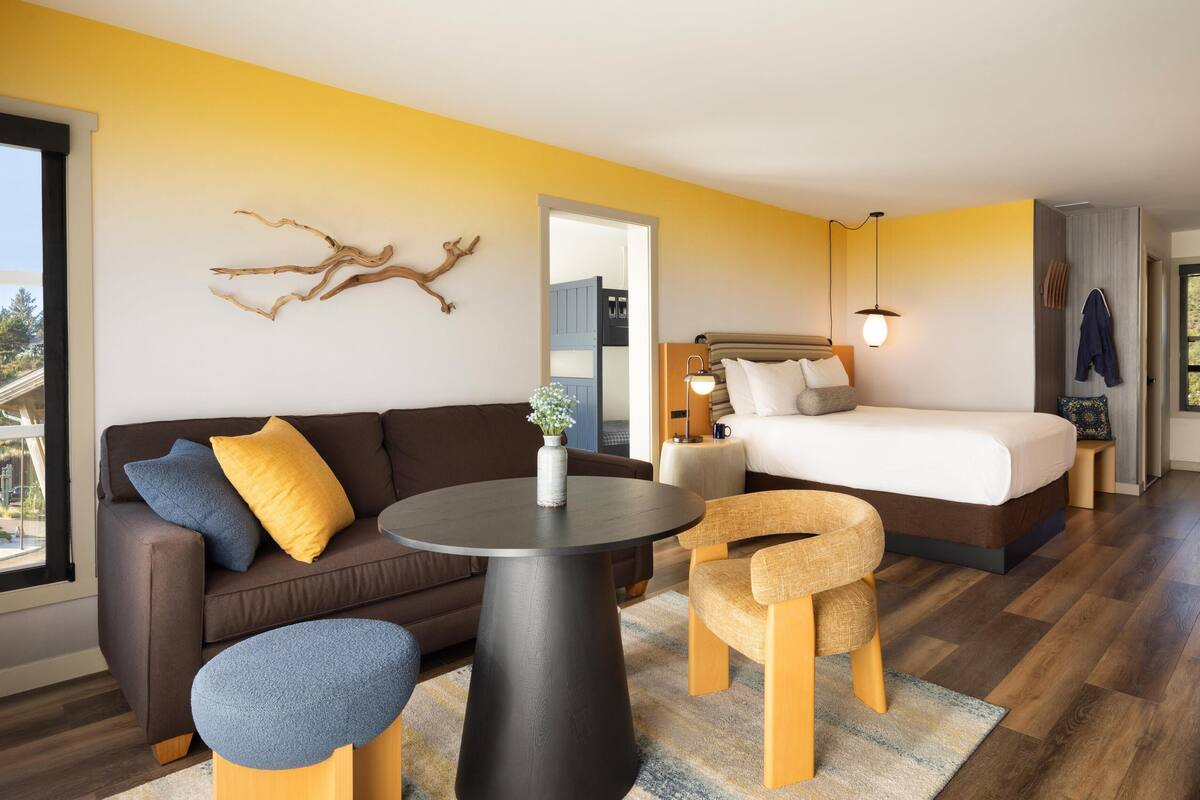 A modern hotel room with a sofa, a round table, a bed, and a view of the outdoors.