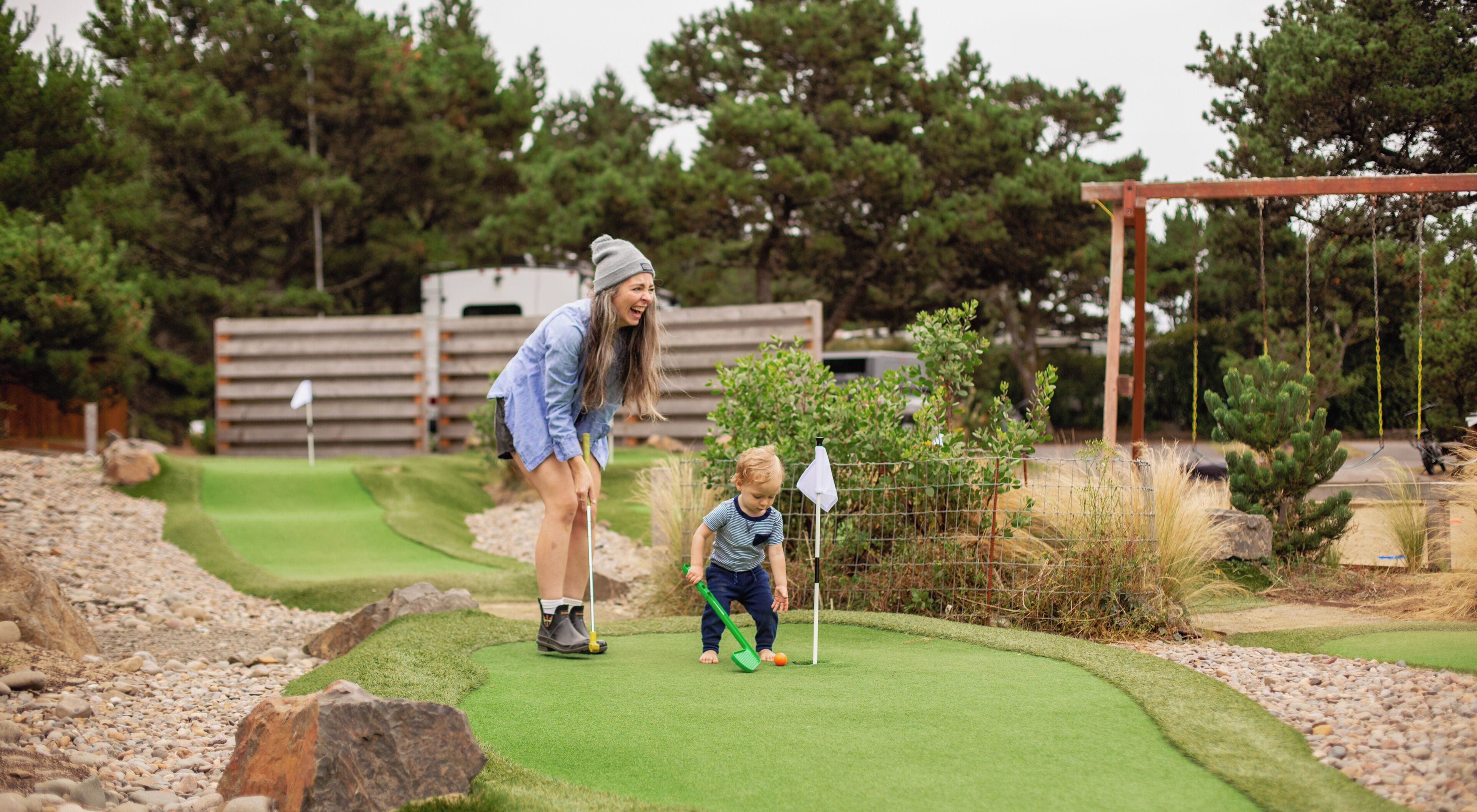 Ein Golfplatz mit Putting Green, Holzzaun und Bäumen im Hintergrund.