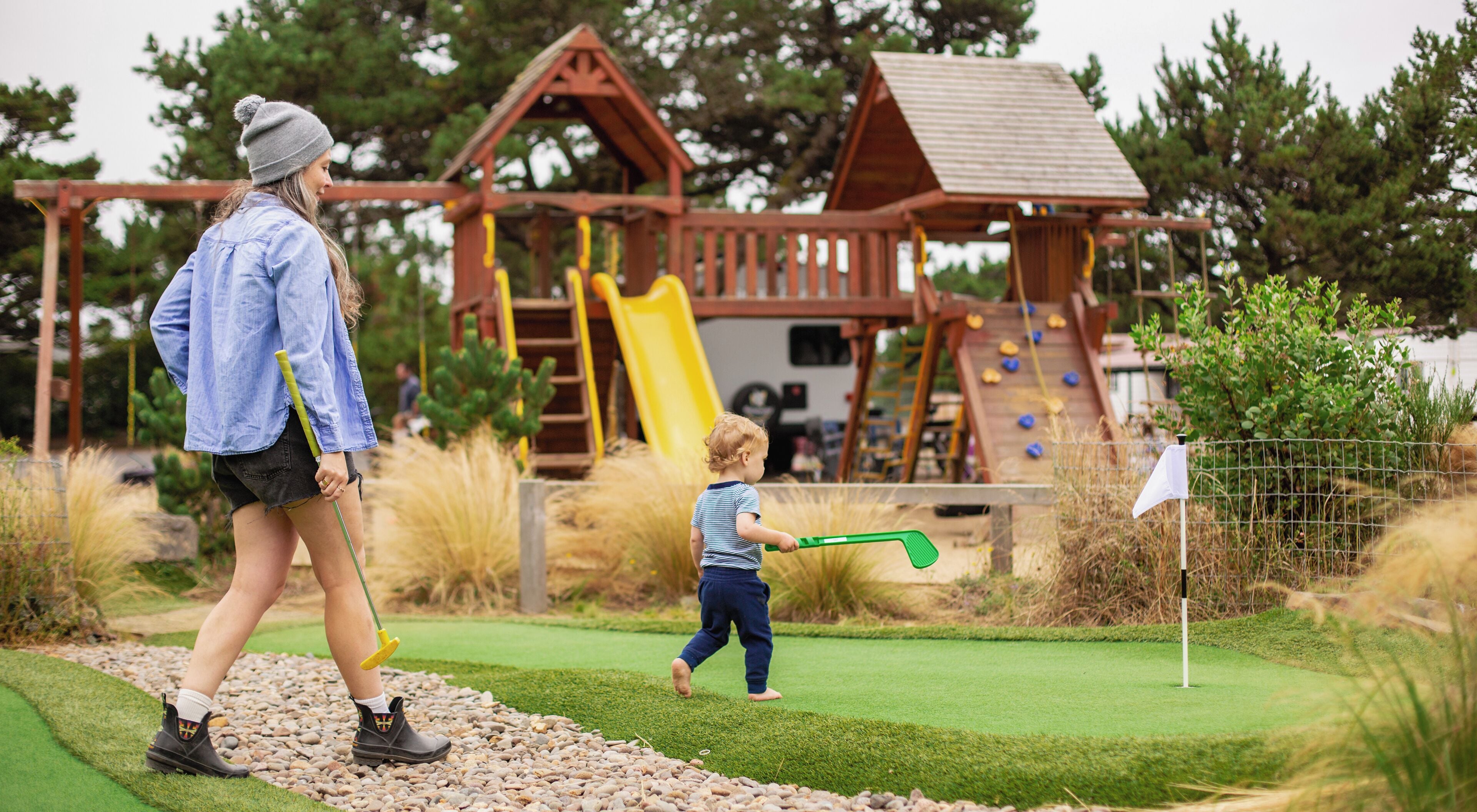 Une aire de jeux avec un toboggan et des structures d’escalade, entourée d’herbe et d’arbres.