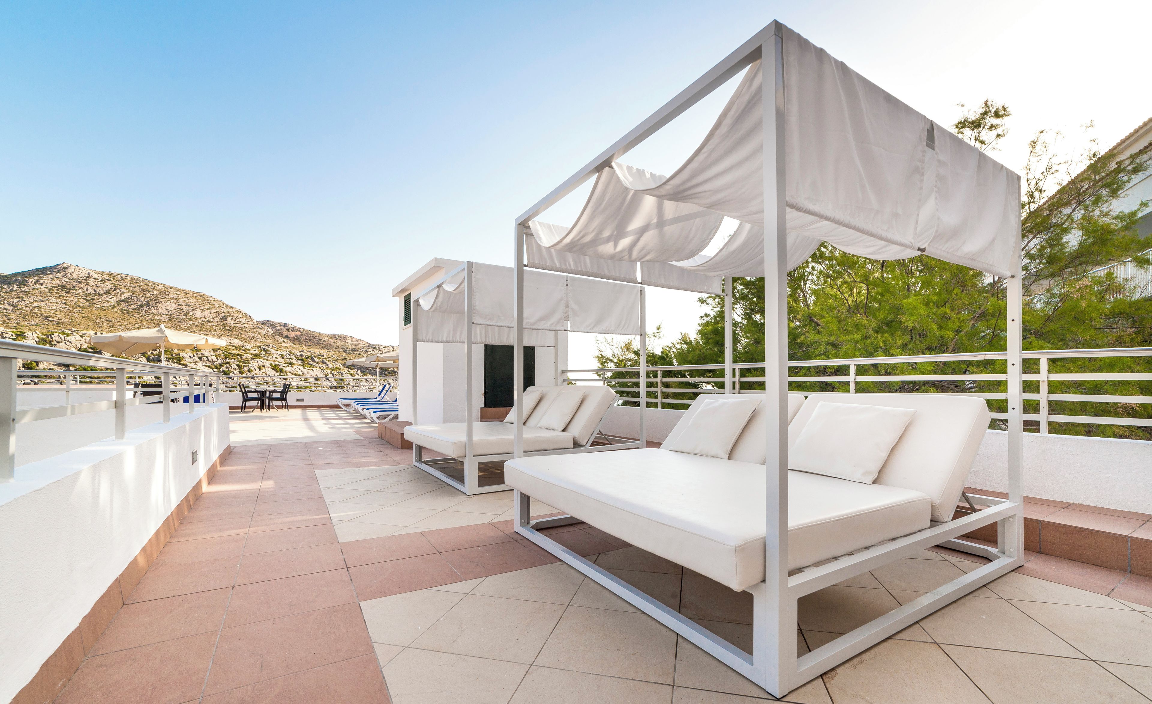 Una terraza en la azotea con toldos blancos, sillones de descanso y vistas a un paisaje montañoso.
