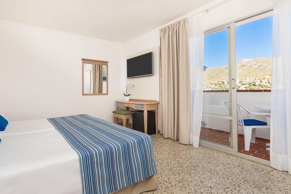 Une chambre d’hôtel avec un lit, un bureau, une télévision et un balcon équipé de chaises.