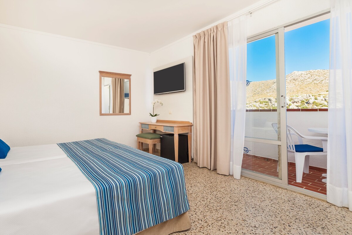 Ein Hotelzimmer mit Bett, Schreibtisch, Fernseher und Balkon mit Stühlen.