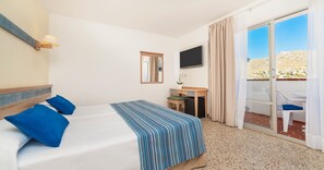 Hotellihuone, jossa on sänky, työpöytä, televisio ja liukuovella varustettu lasiterassi, joka johtaa ulkotilaan.